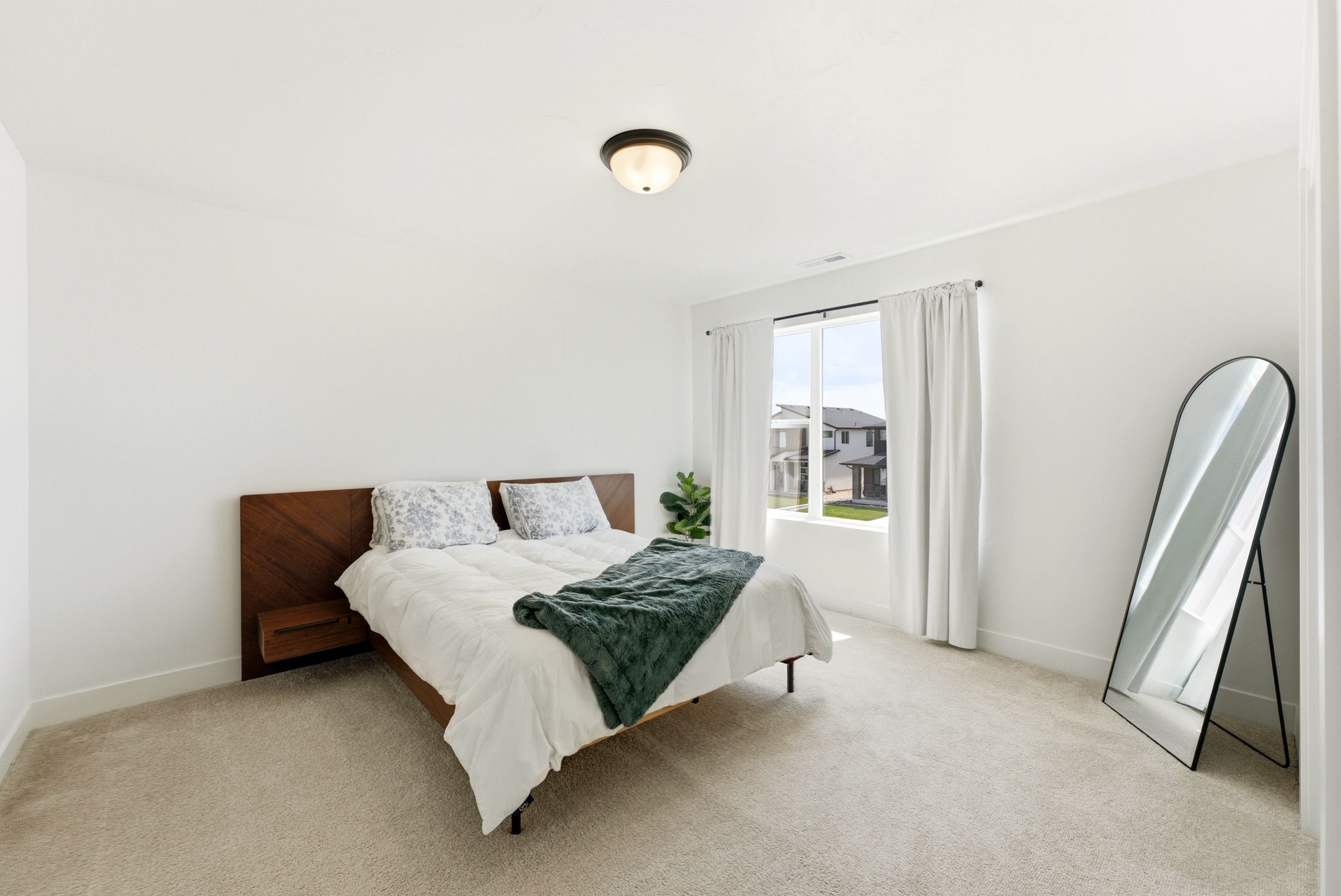 Carpeted bedroom featuring a large window with white curtains, a flush-mount ceiling light fixture, and white painted walls