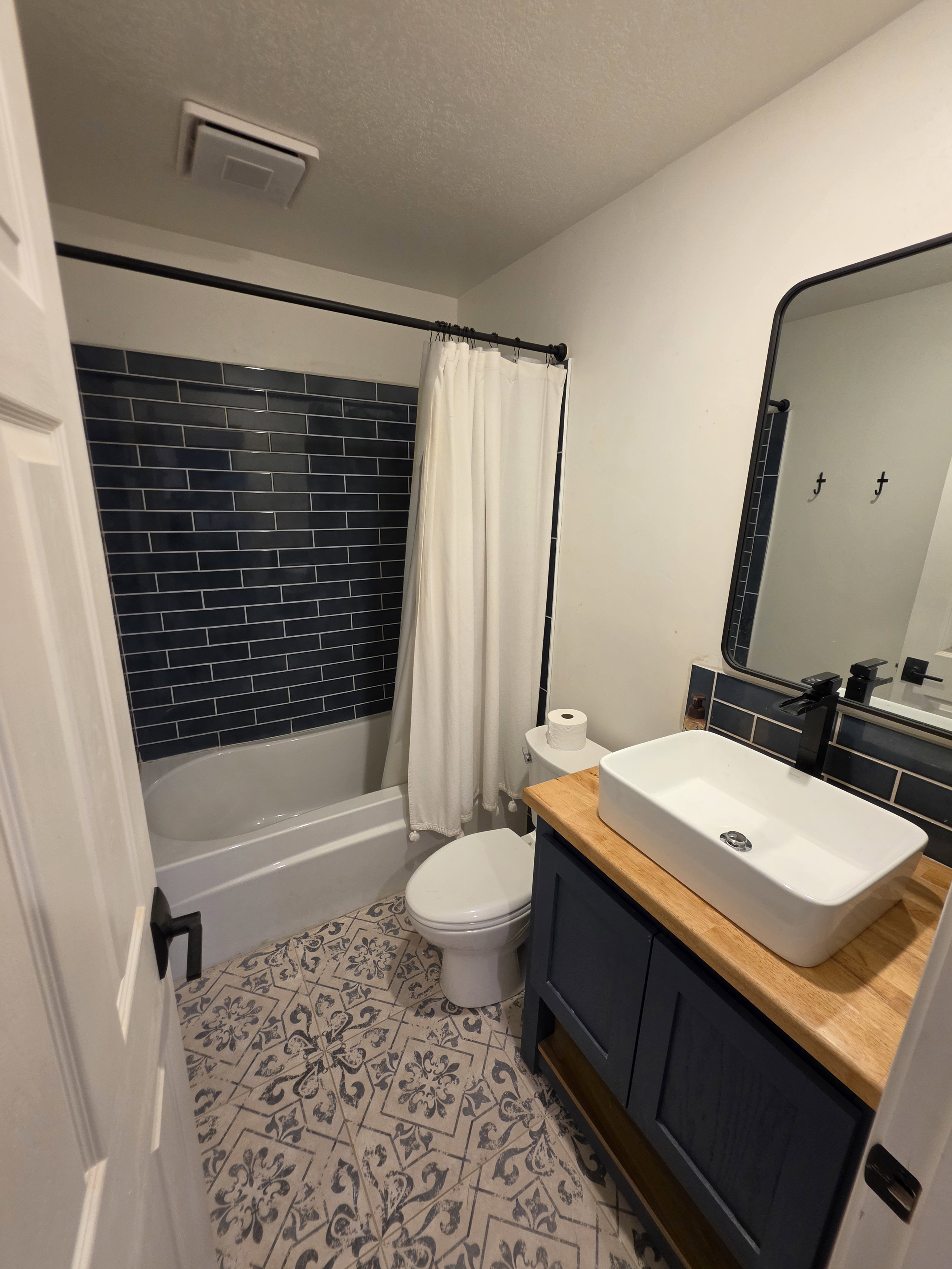 Modern bathroom featuring patterned floor tiles and a deep blue subway tile surround