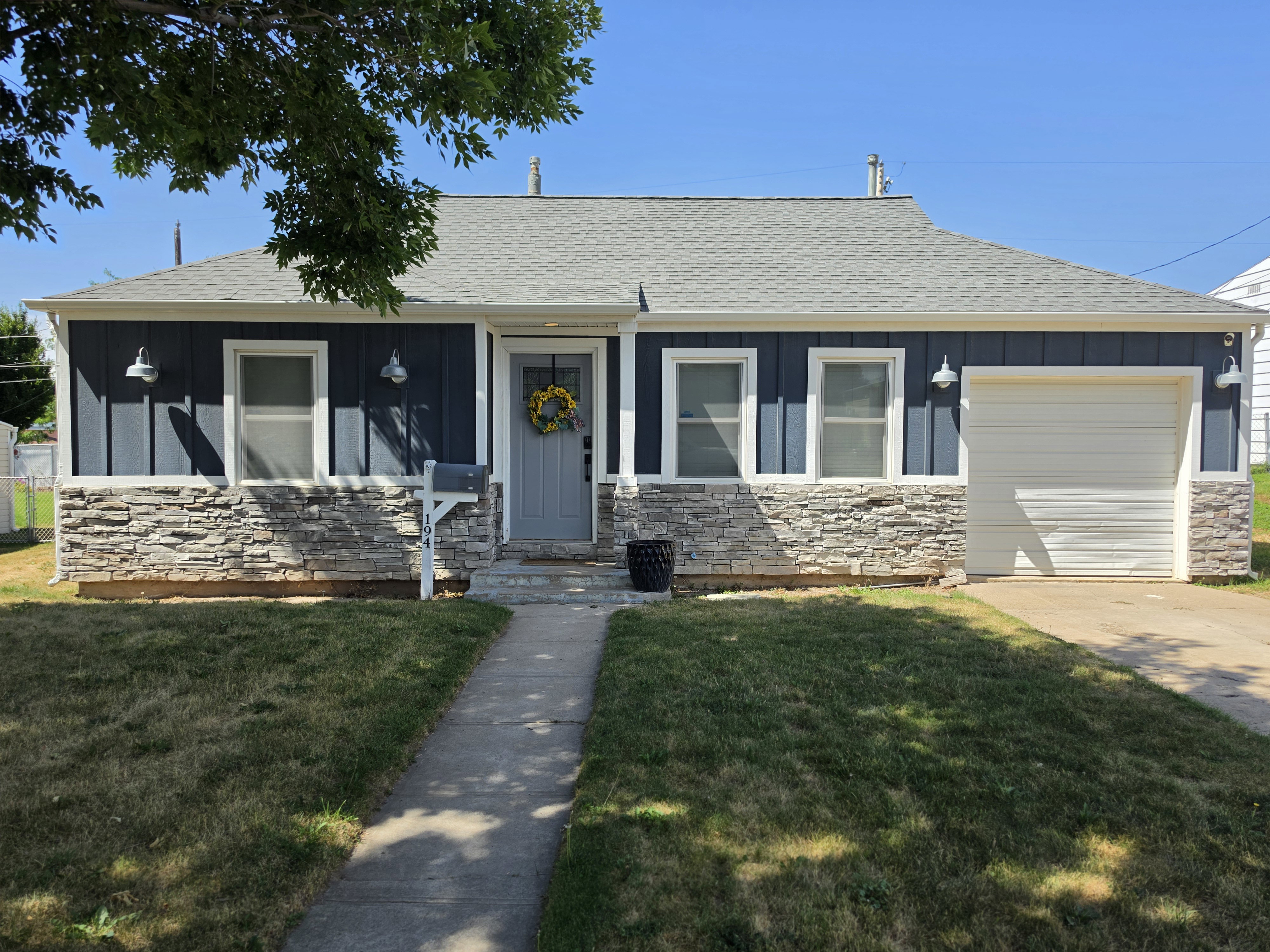 Exterior featuring blue board and batten siding, stone veneer accents, a single-car garage, and a concrete driveway