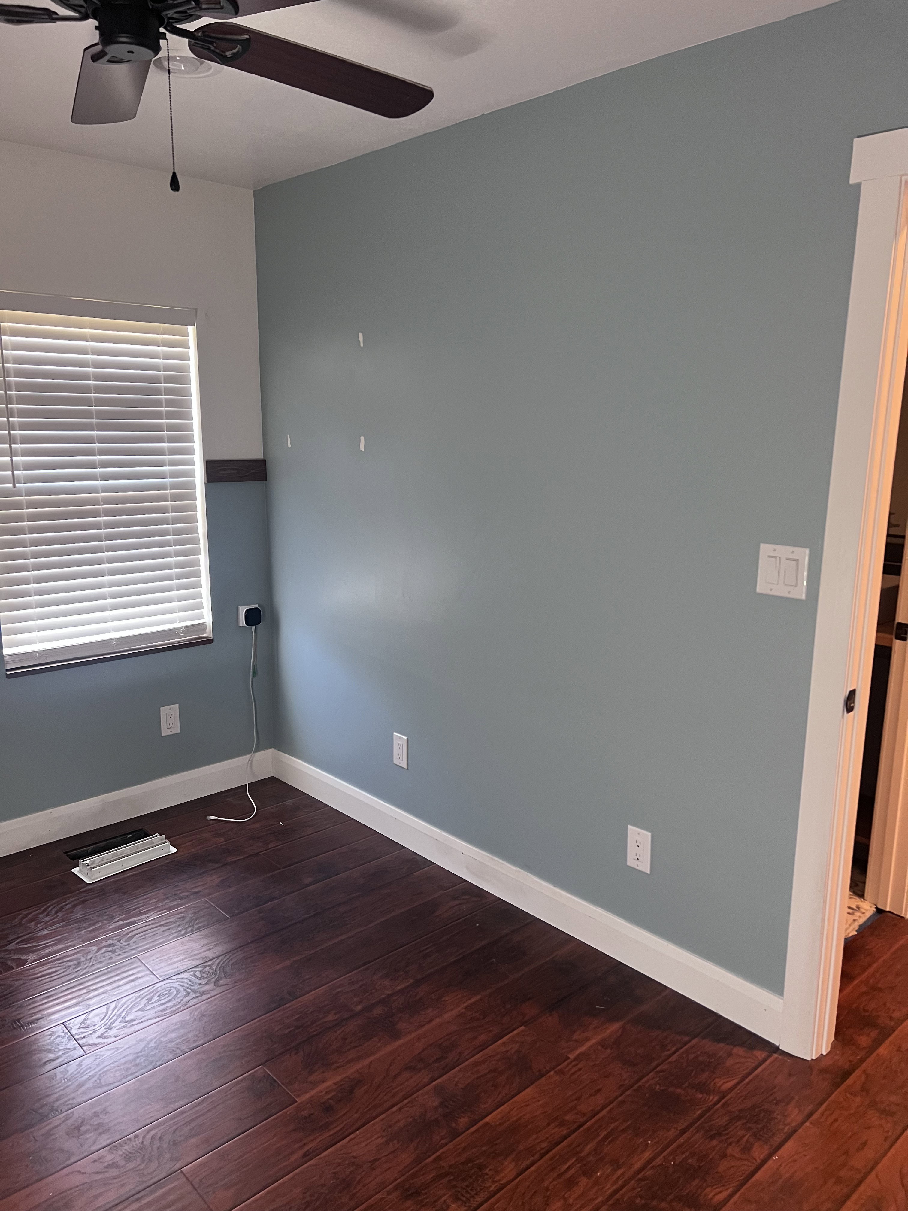 Room featuring wood-finish flooring, a ceiling fan with light, white baseboards, and a window with blinds