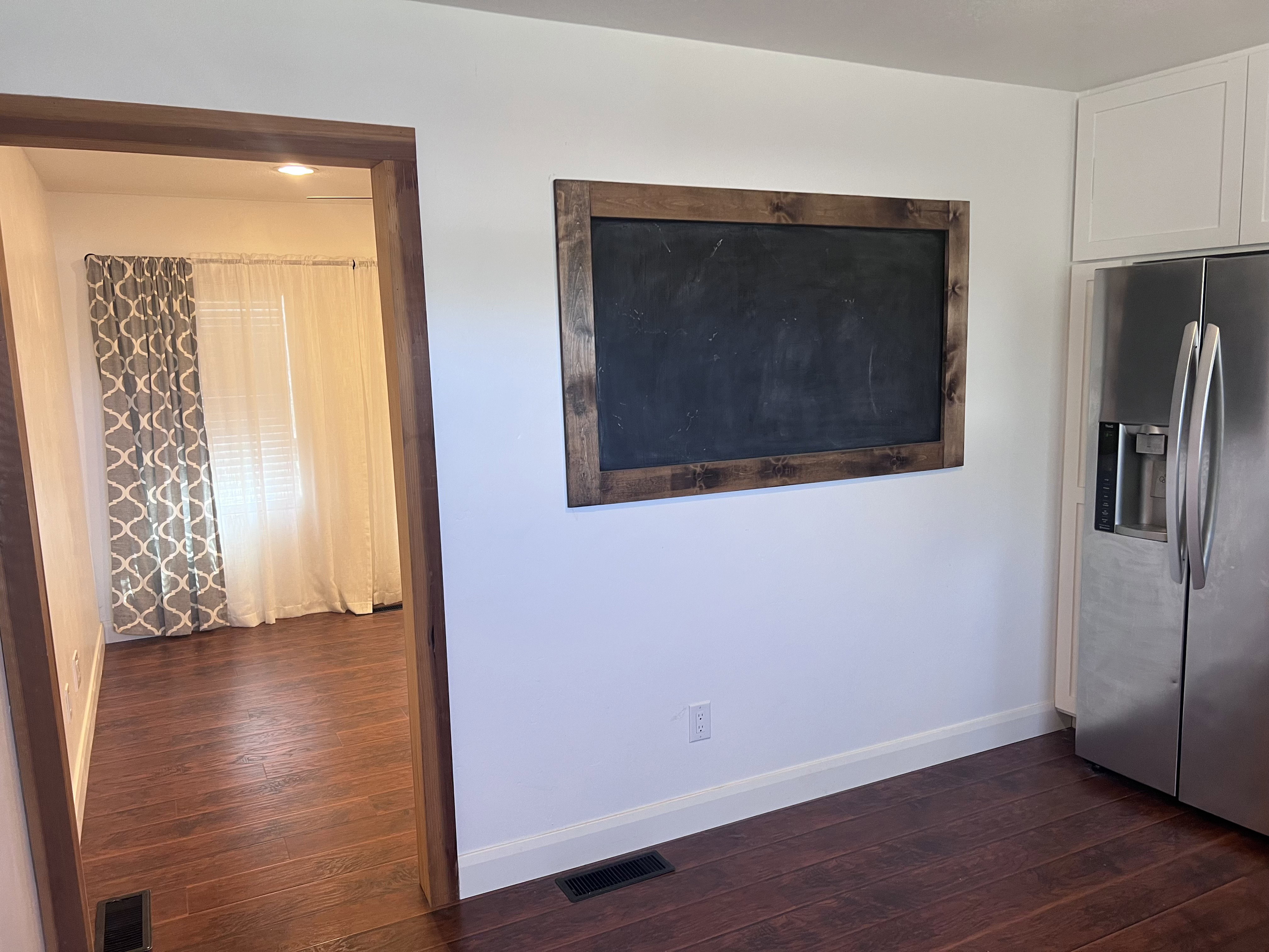Kitchen wall featuring a framed chalkboard, stainless steel refrigerator, and white upper cabinetry