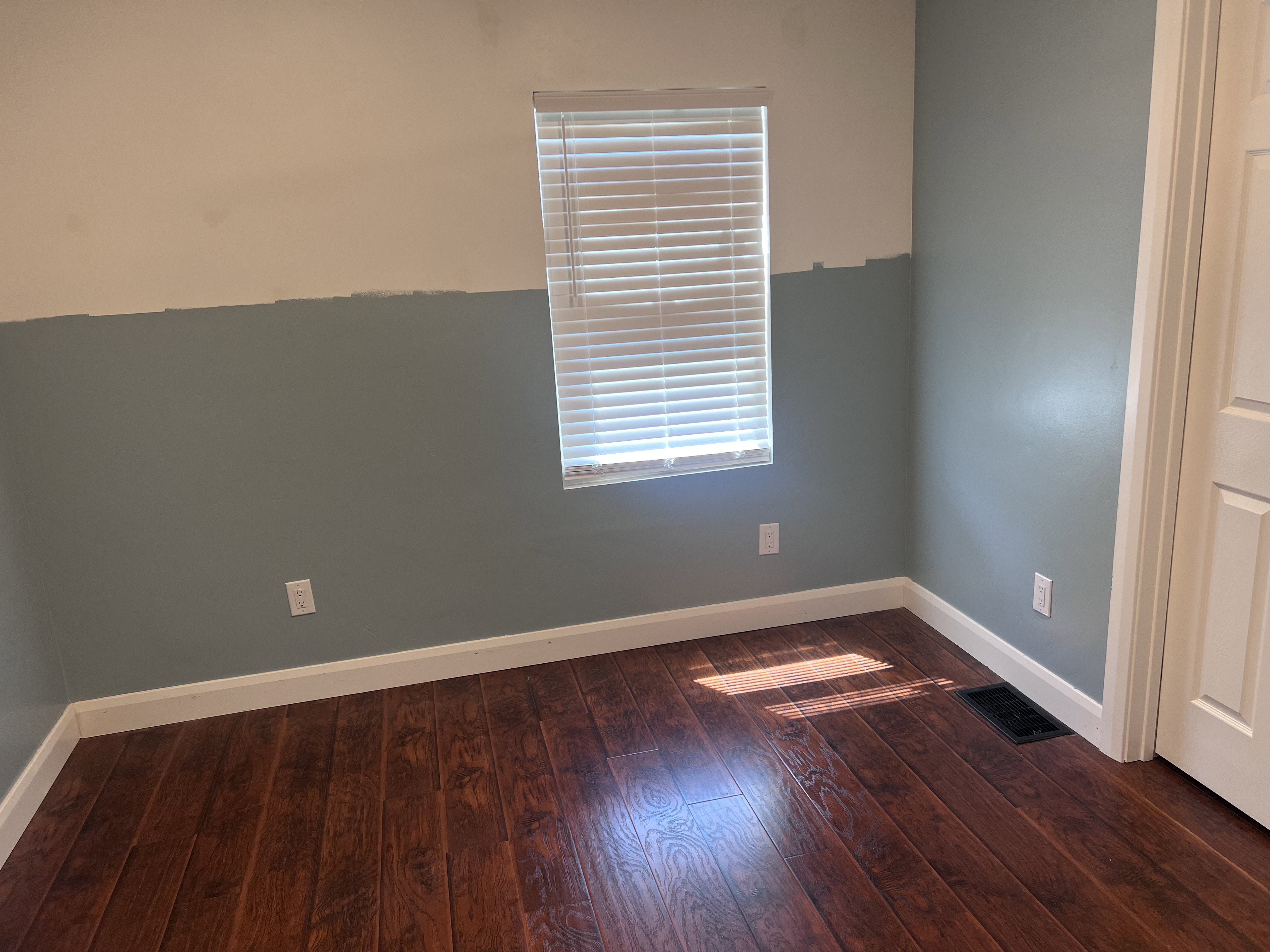 Room with wood-finish flooring, white baseboards, and two-tone painted walls