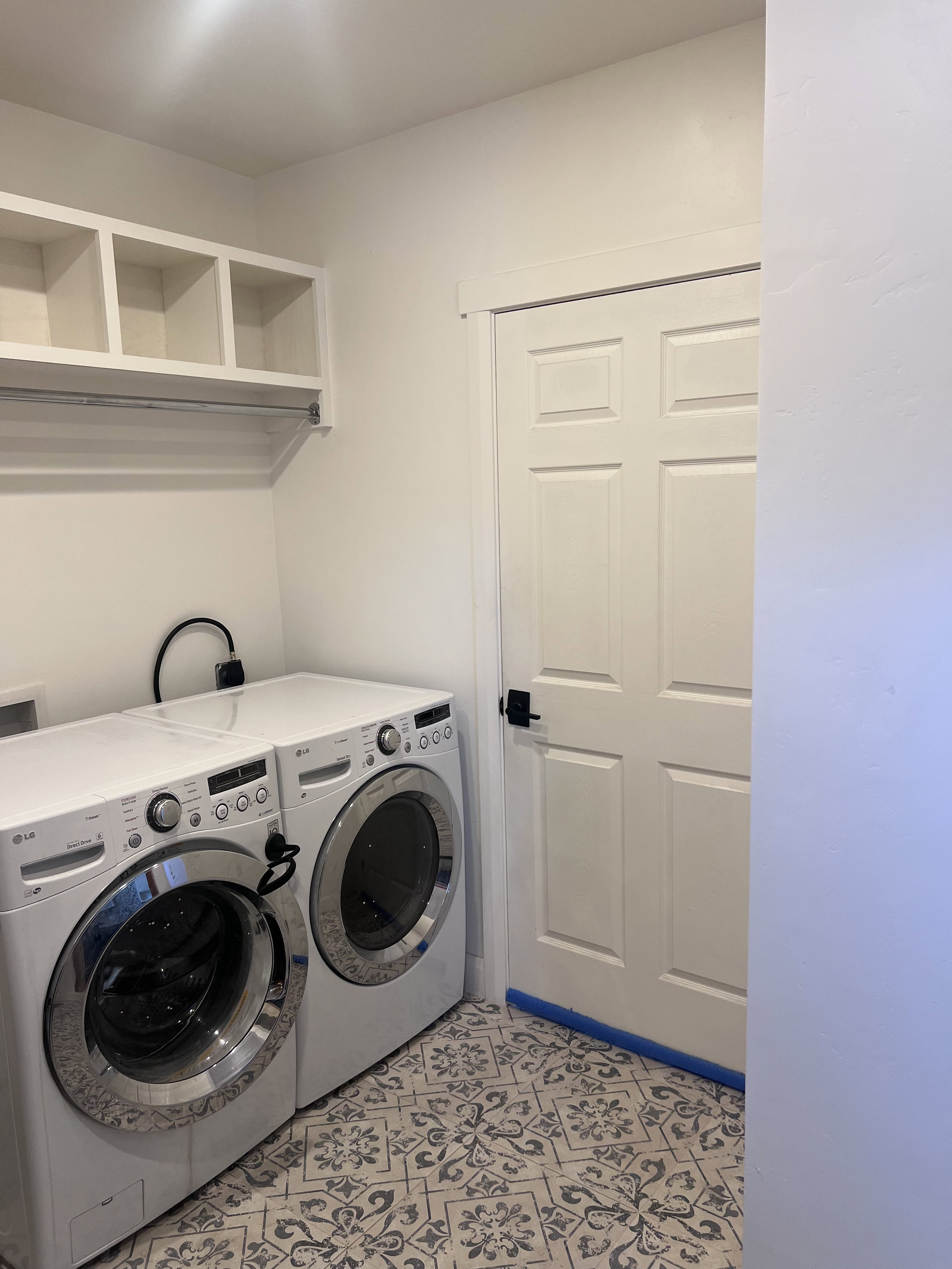 Laundry area featuring patterned floor tile, overhead shelving, and a hanging rod