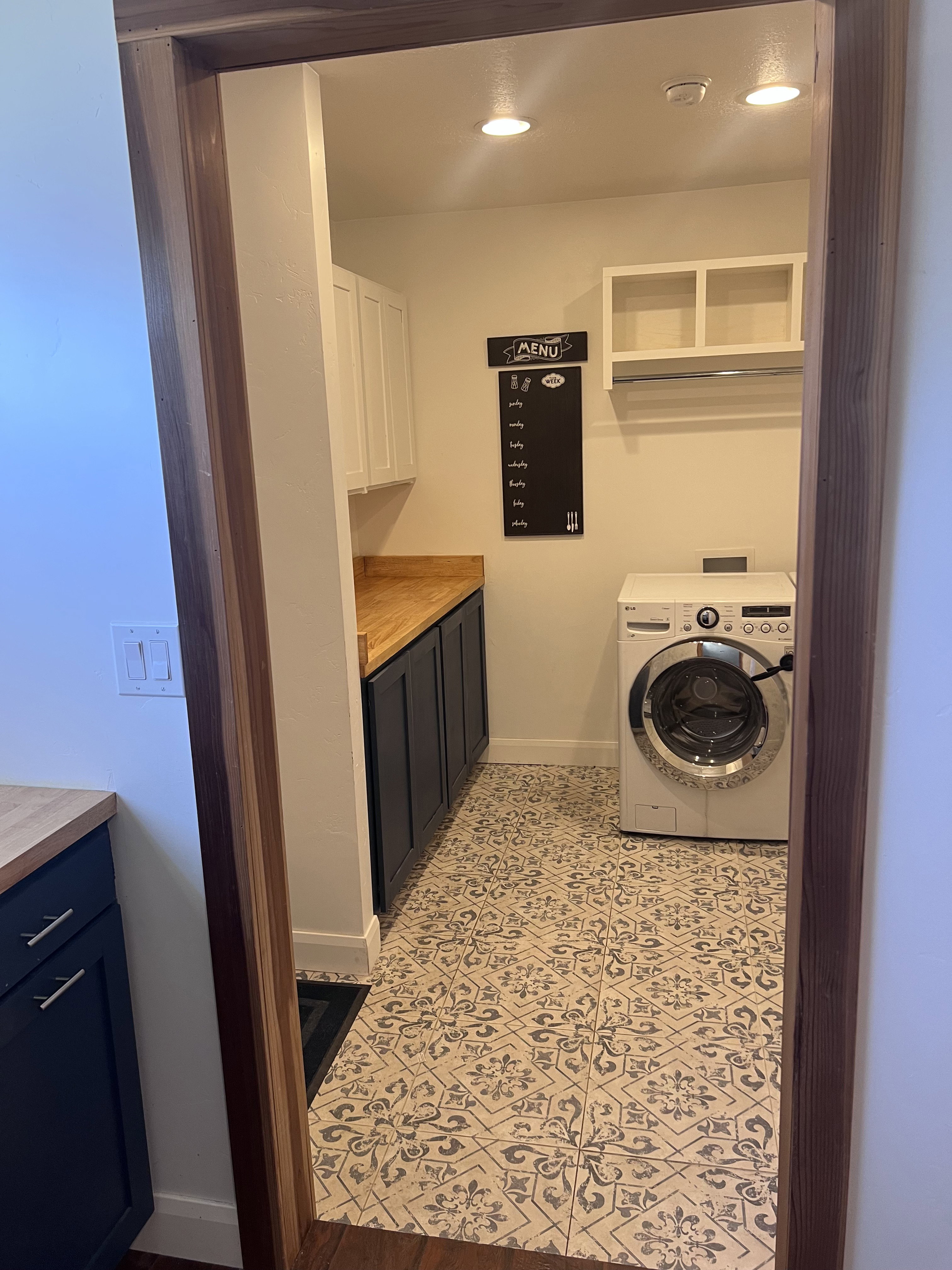 Utility room featuring patterned tile flooring, wood-finish countertops, dark base cabinetry, white upper cabinetry, and recessed lighting