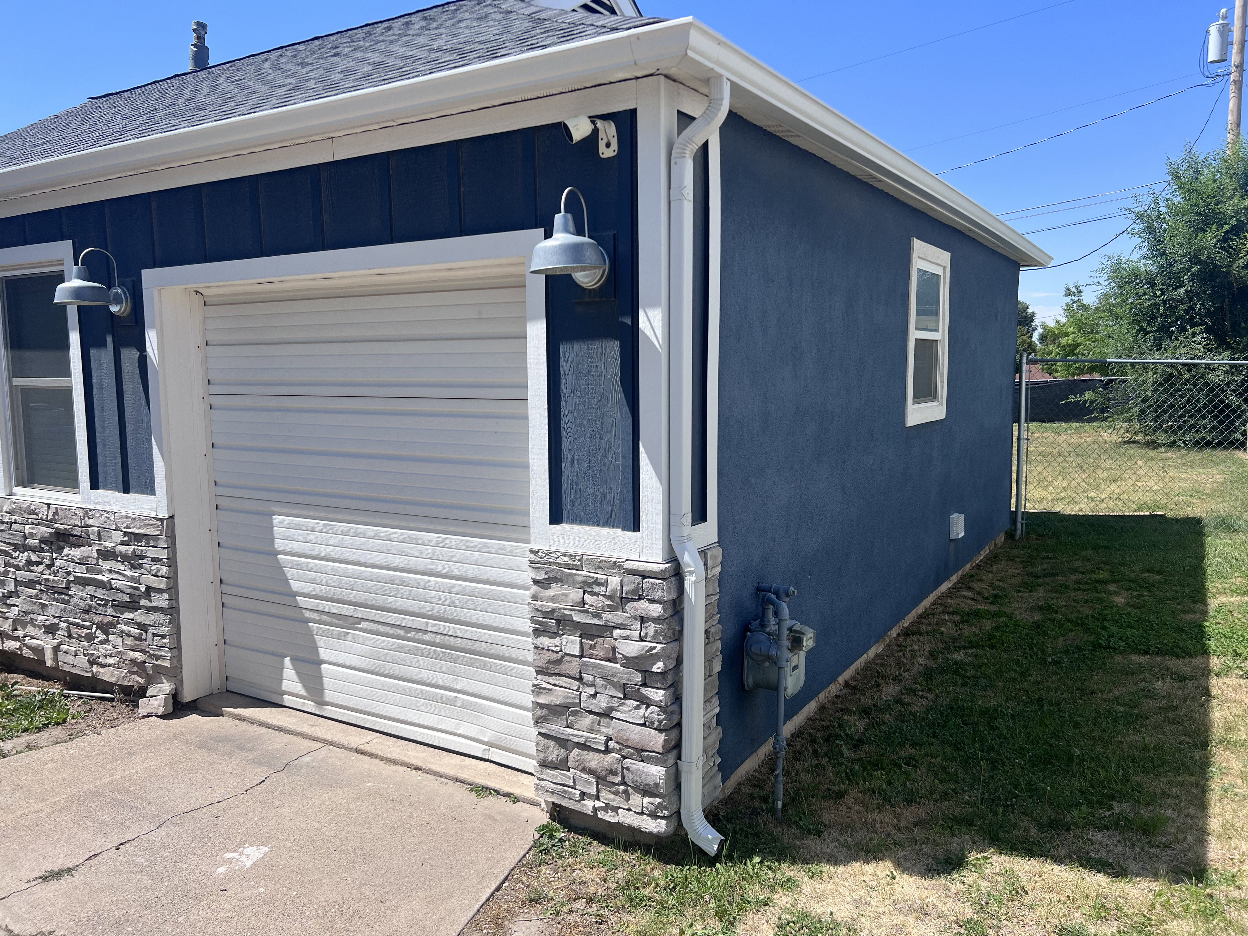 Detached structure featuring a single garage door, blue siding, stone-finish wainscoting, and a shingle roof