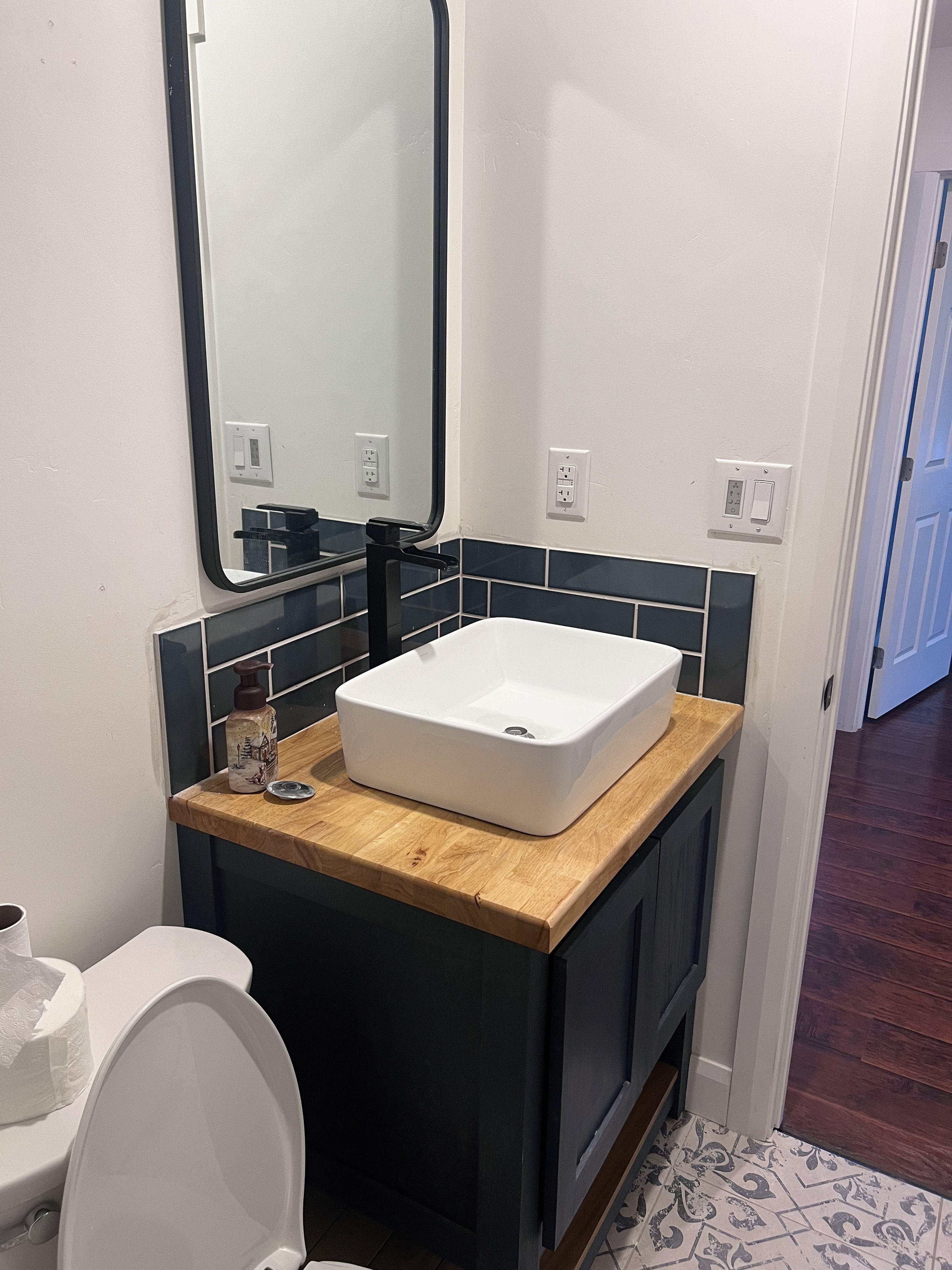 Bathroom featuring a dark wood-finish vanity with a butcher block style countertop, a white vessel sink, and a matte black faucet
