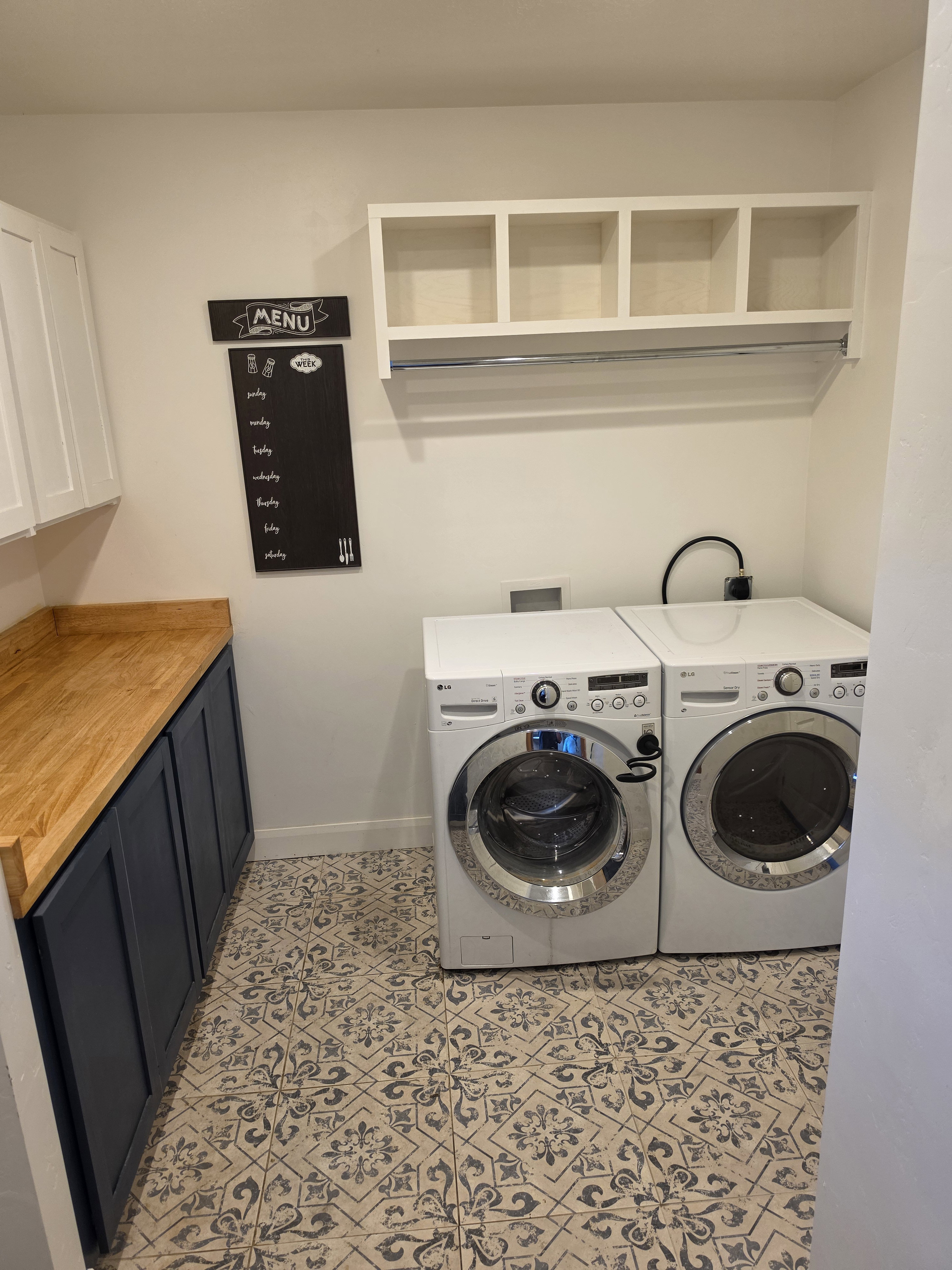 Laundry area featuring patterned floor tiling, built-in lower cabinetry with a wood countertop, and upper open shelving with a hanging rod