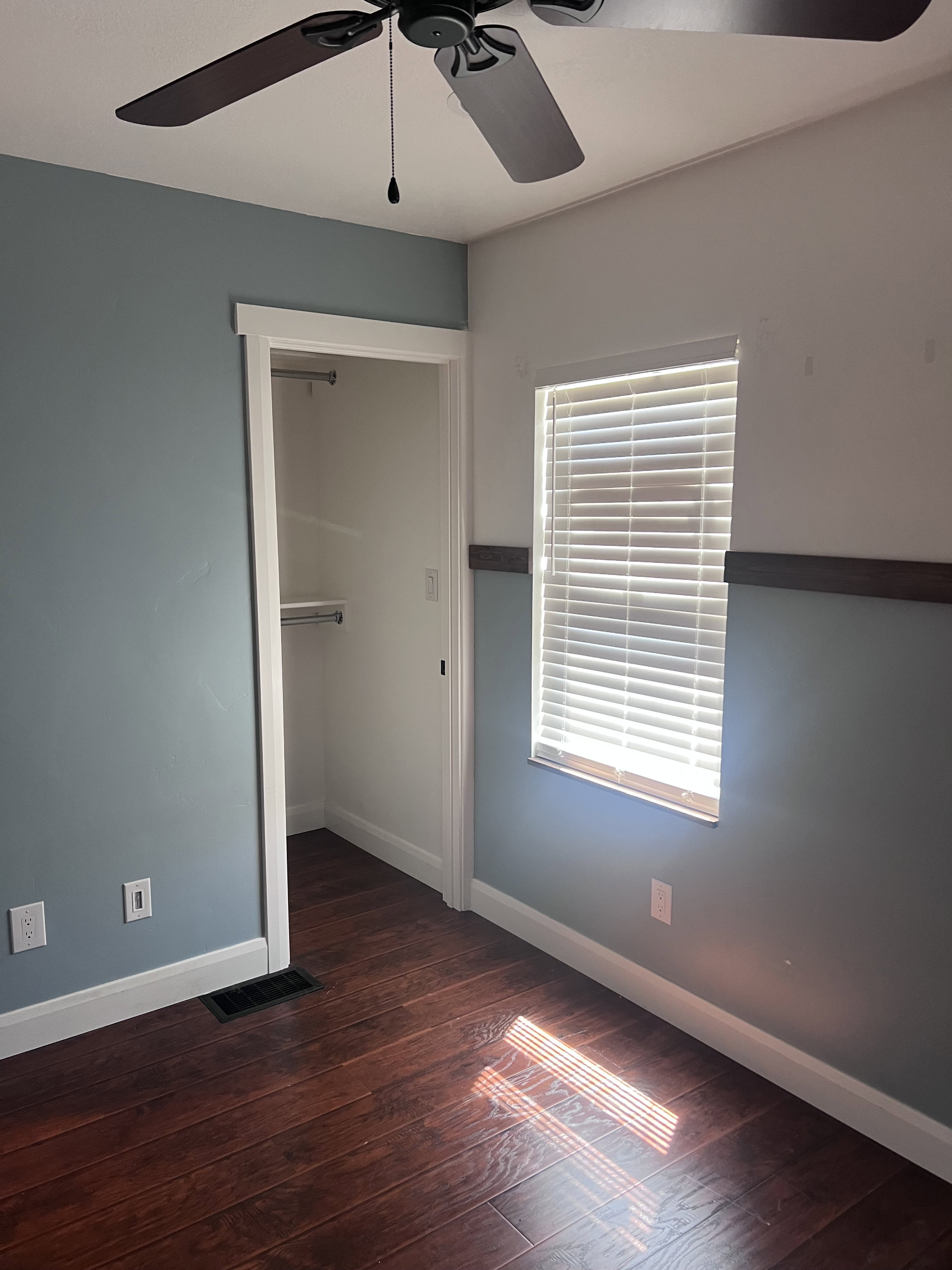 Interior room featuring wood-finish flooring, a ceiling fan, and a window with horizontal blinds