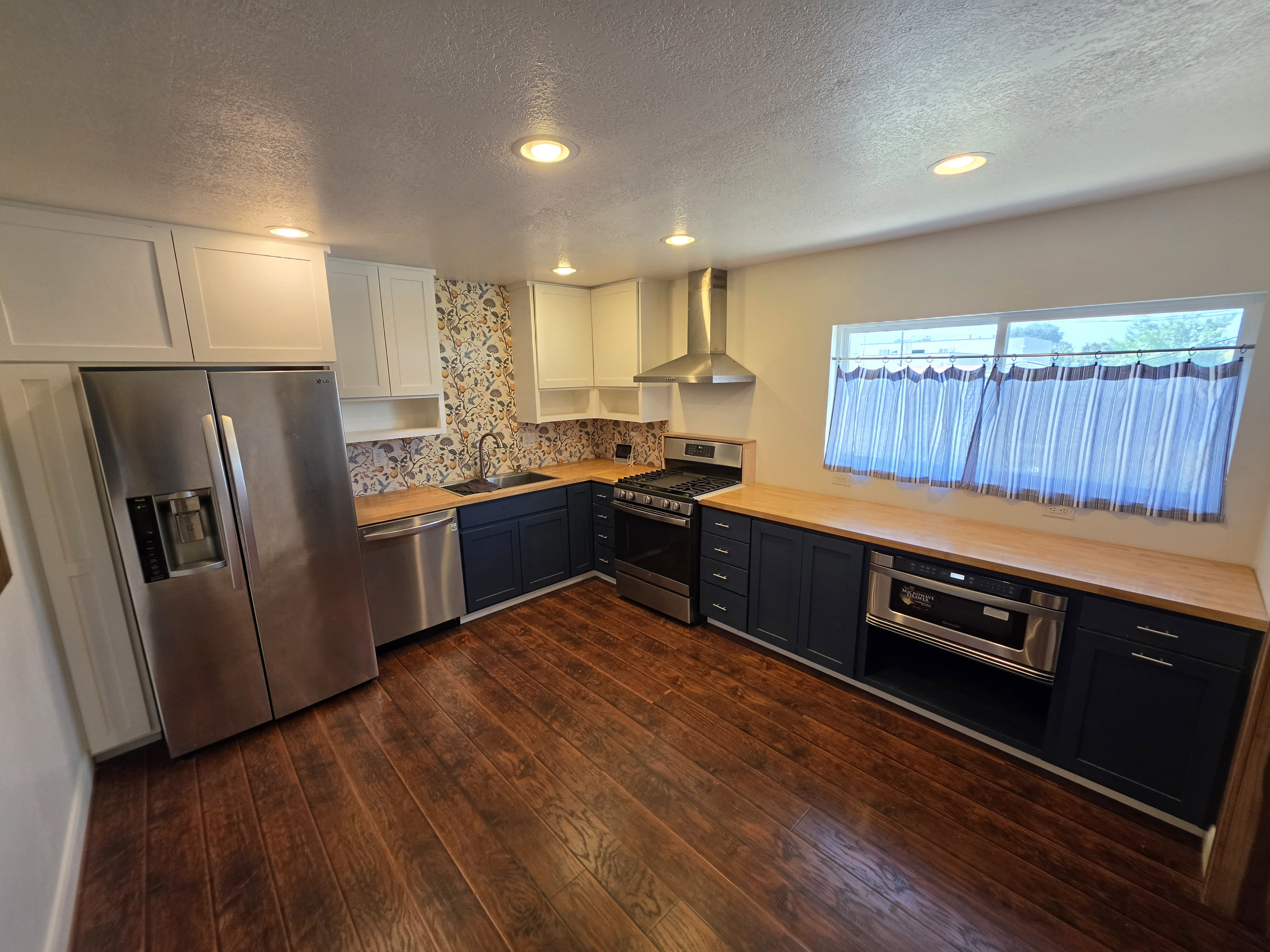 Kitchen featuring wood-finish flooring, two-tone cabinetry with white upper and dark lower cabinets, light wood countertops, and a patterned backsplash