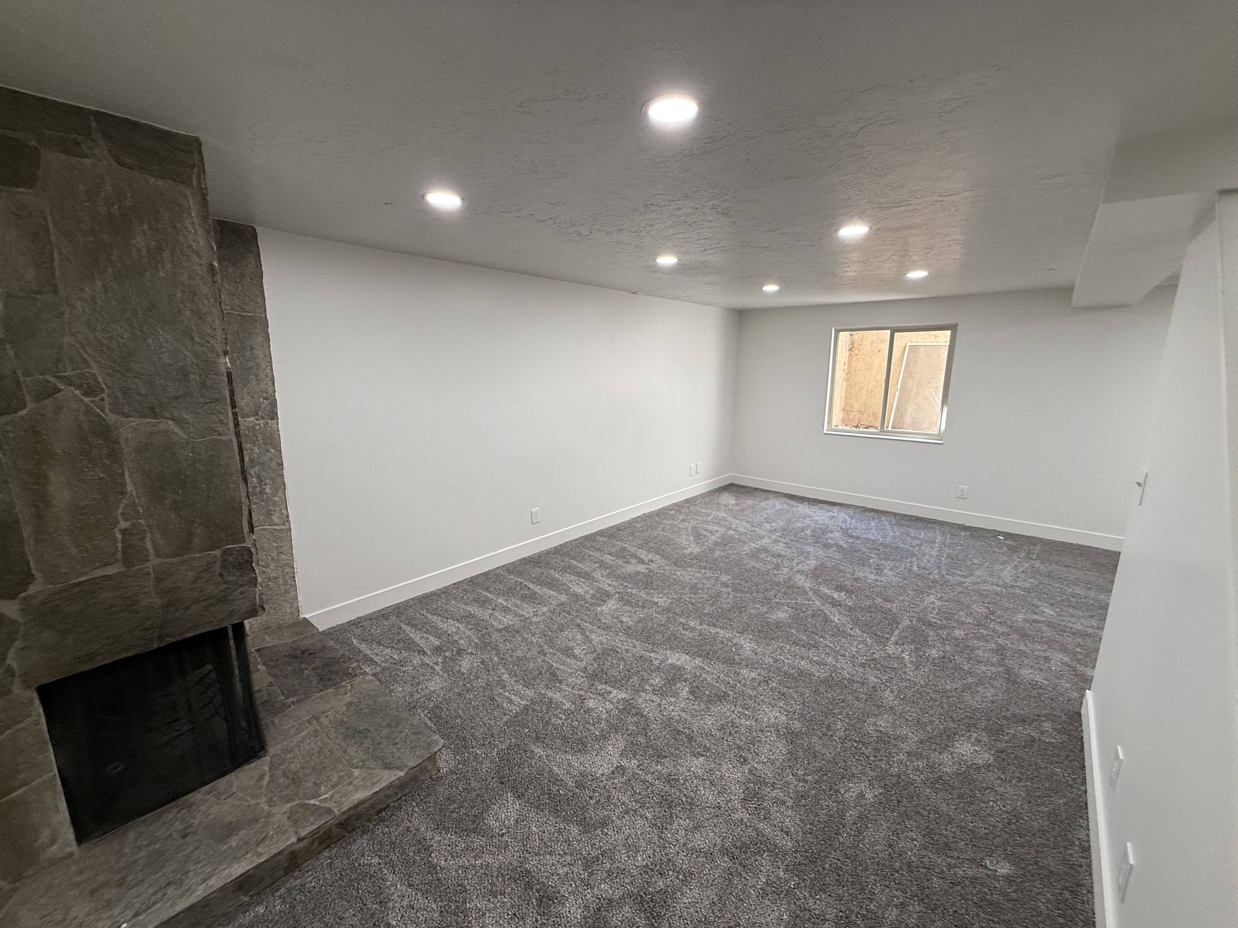 Spacious room featuring a stone-clad fireplace with a hearth, recessed lighting, neutral wall tones, and plush patterned carpeting