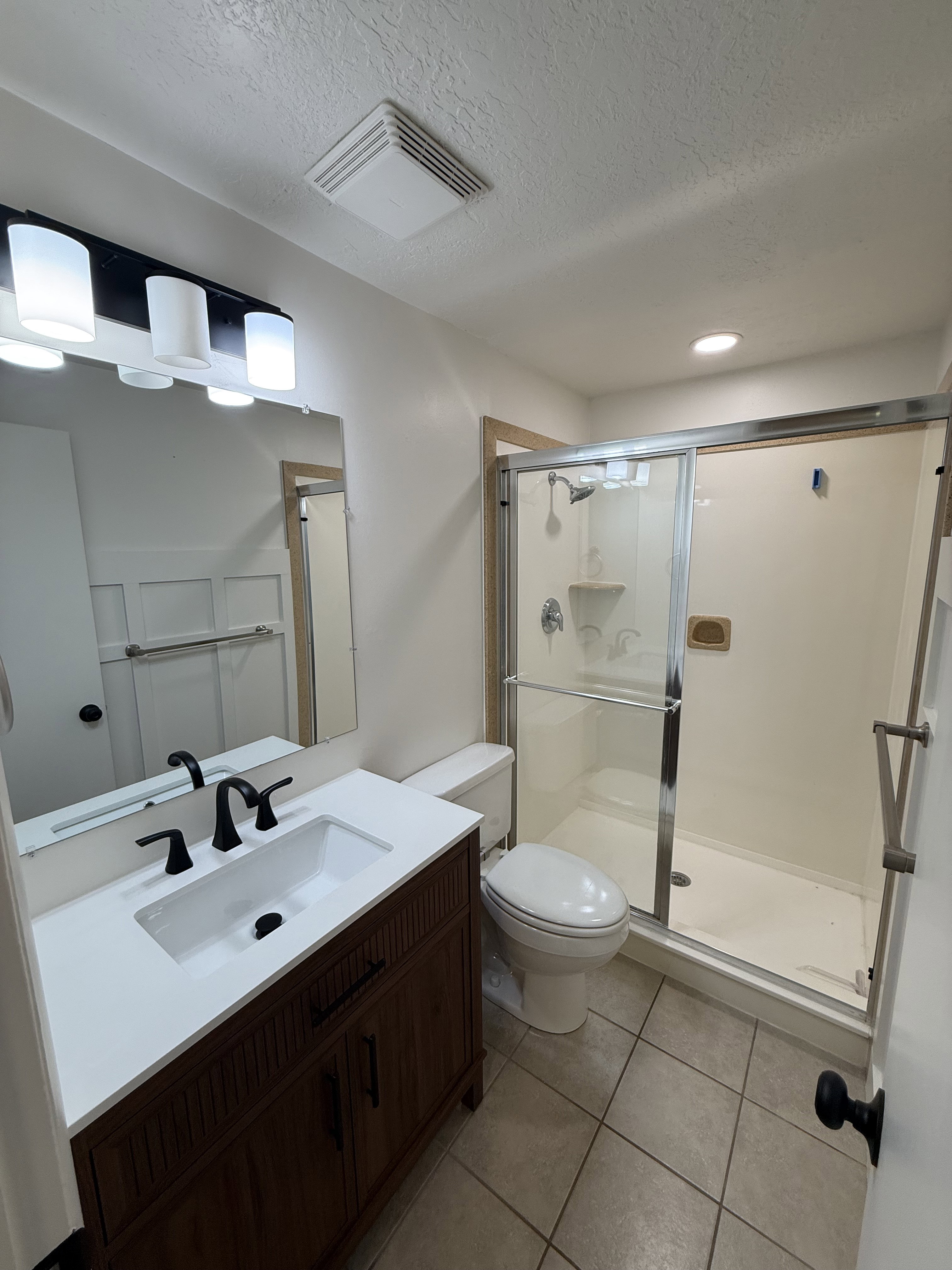 Bathroom featuring a dark wood-finish vanity with a white countertop and integrated sink, matte black faucet, and a frameless mirror