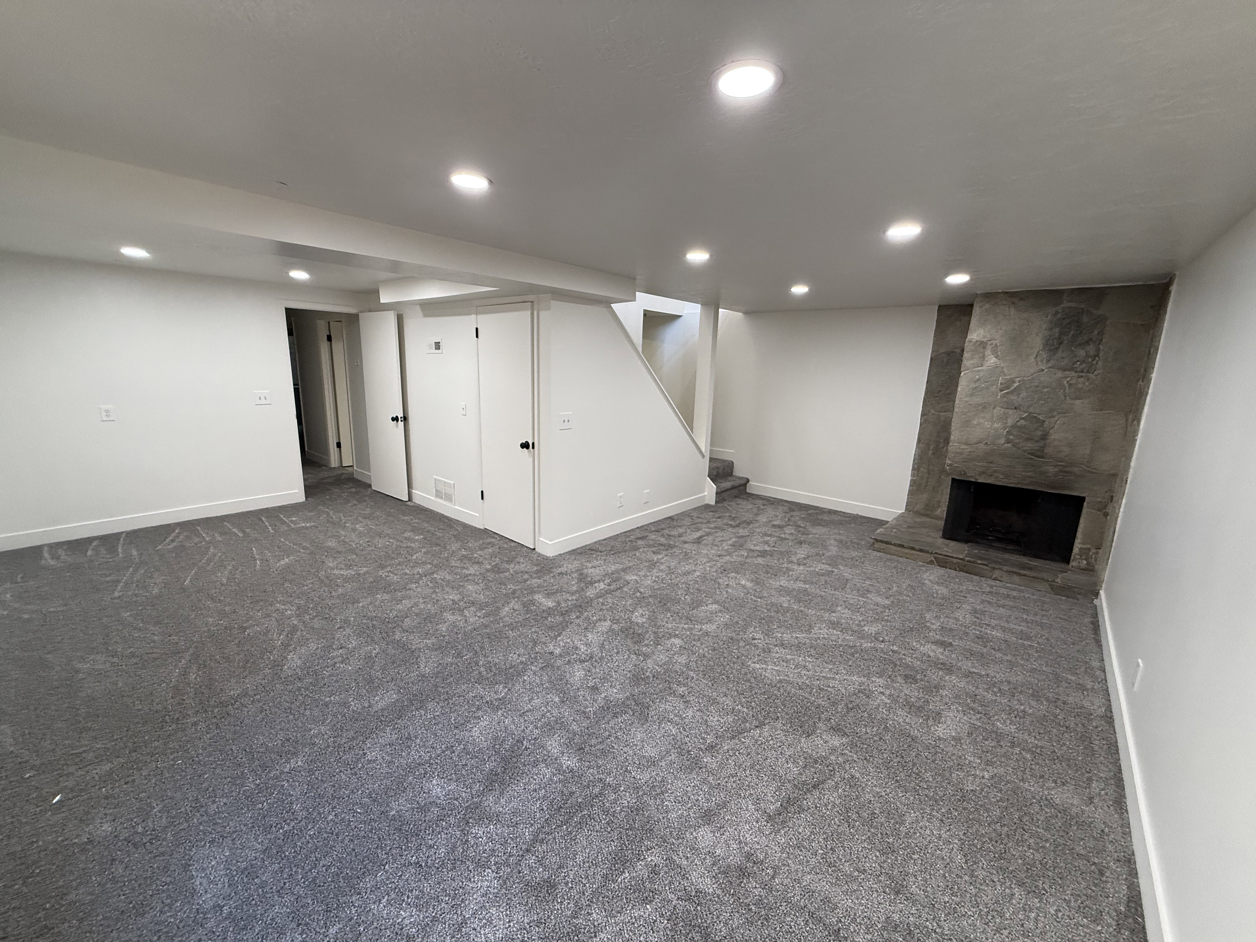 Spacious room featuring gray patterned carpet, recessed lighting, white walls, and a stone-clad fireplace