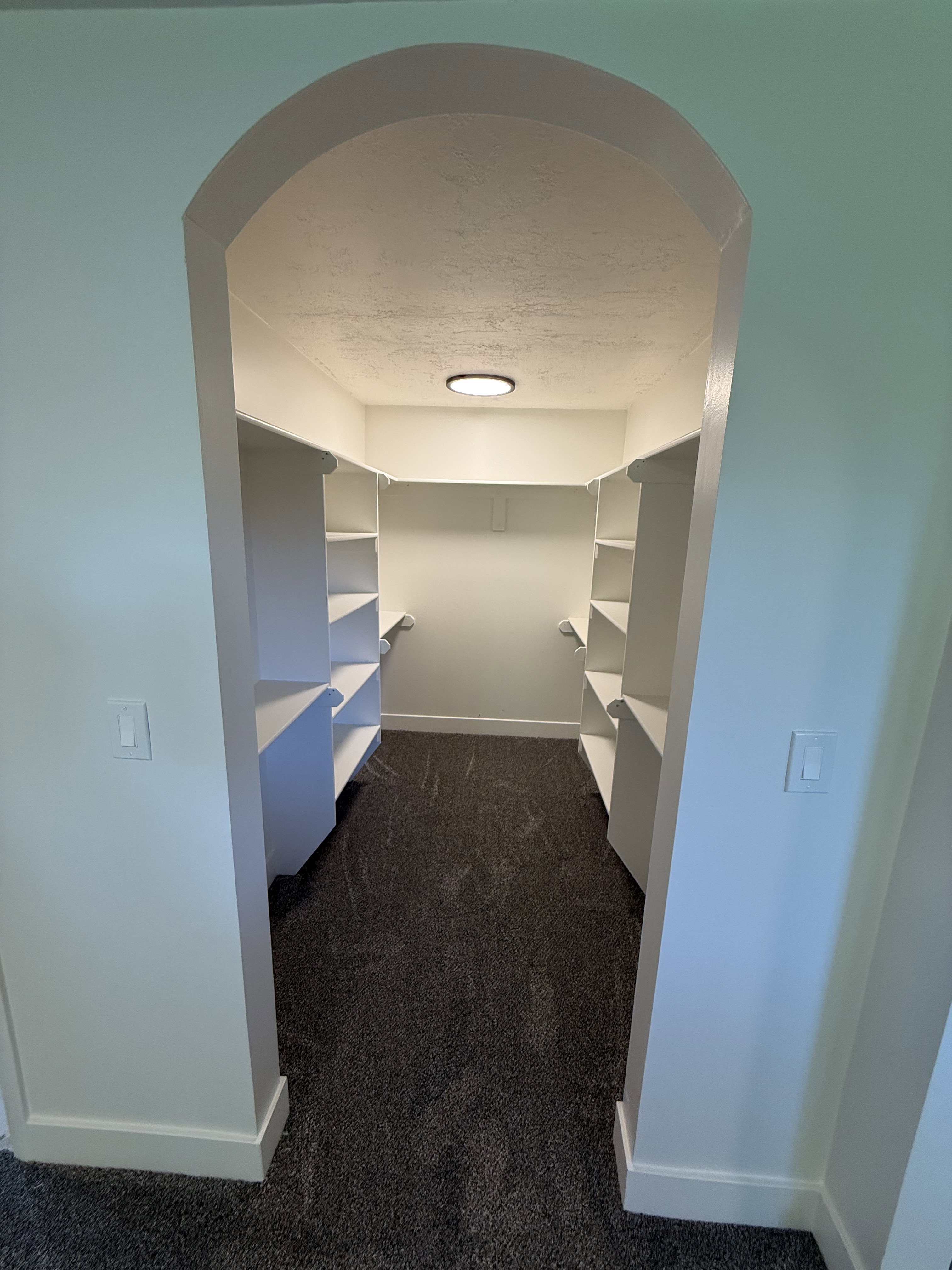 Arched entryway leading into a walk-in closet featuring built-in shelving, dark gray carpet, and recessed lighting