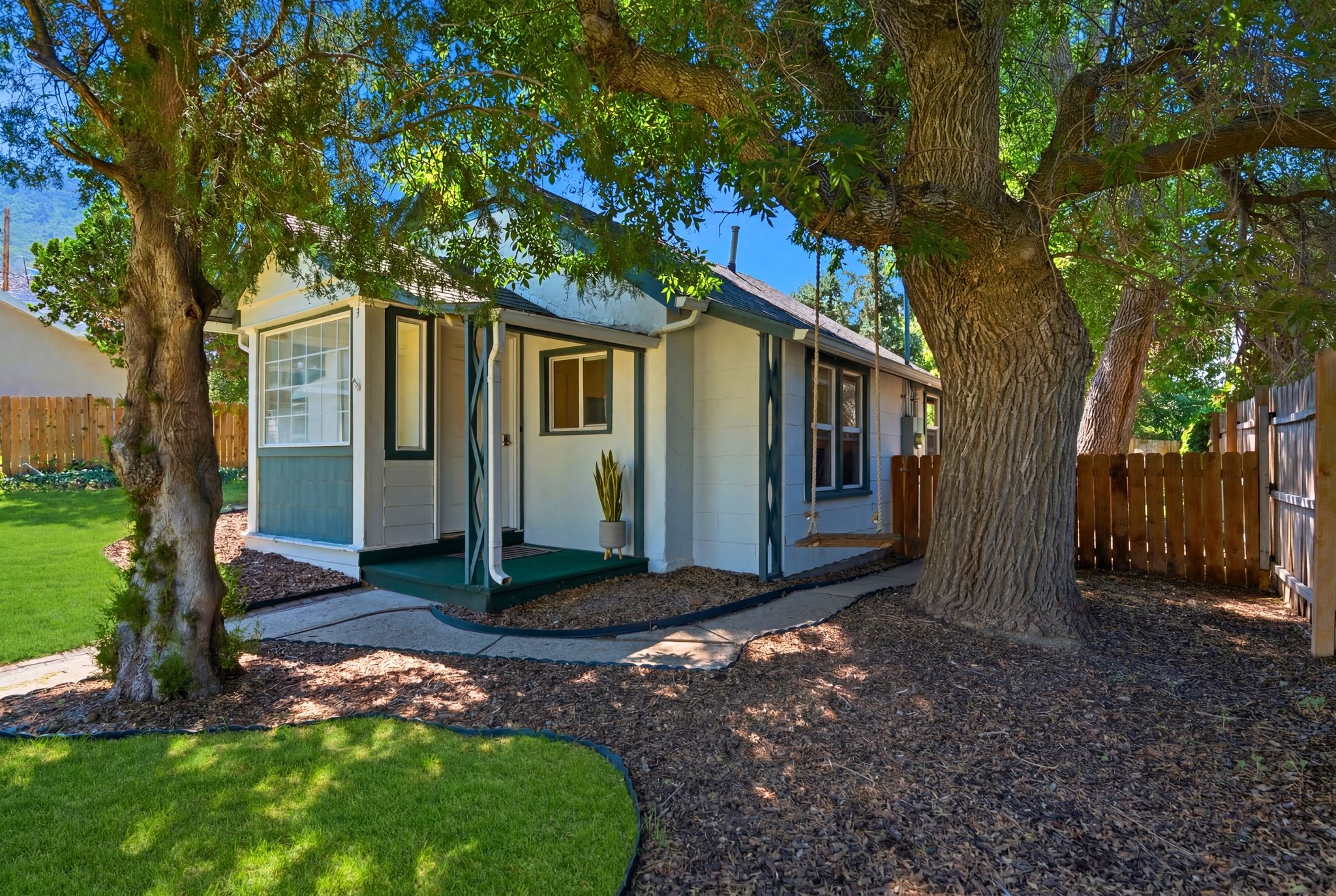 White and green exterior with a covered porch entry, bay window, and a wood privacy fence