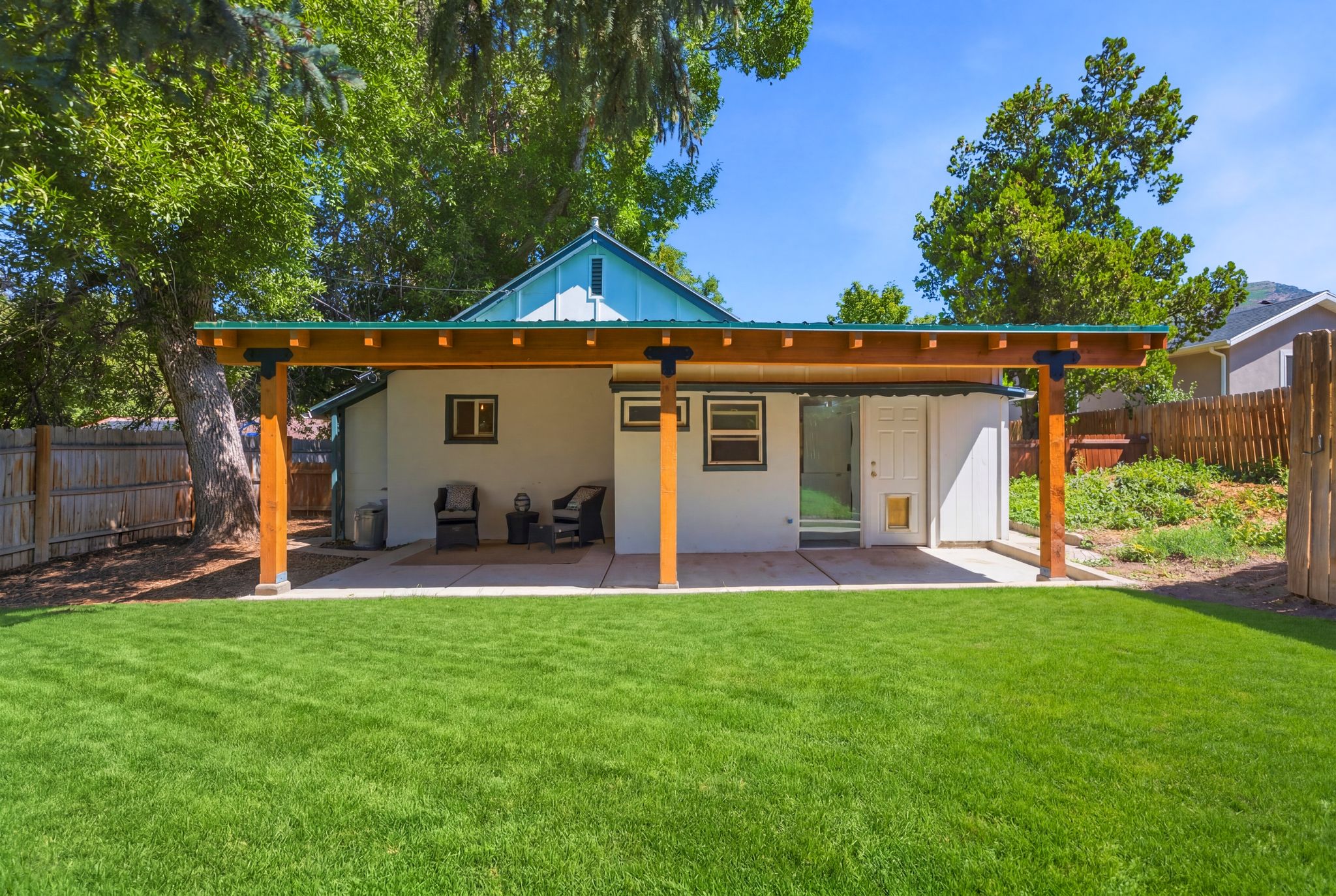 Spacious backyard featuring a covered patio with exposed wood beams, a generous lawn area, and a privacy fence