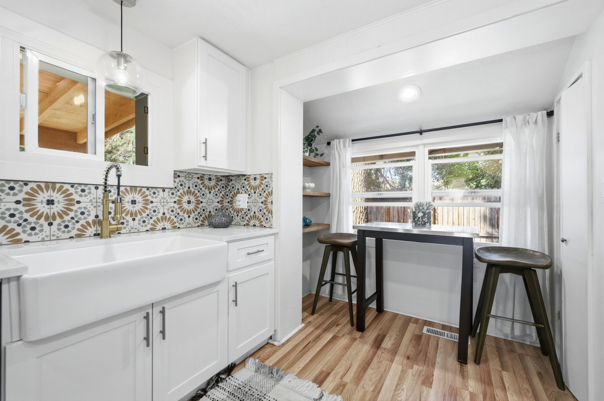 Kitchen featuring a farmhouse sink with a gooseneck faucet, patterned tile backsplash, white shaker cabinetry, and wood-finish flooring