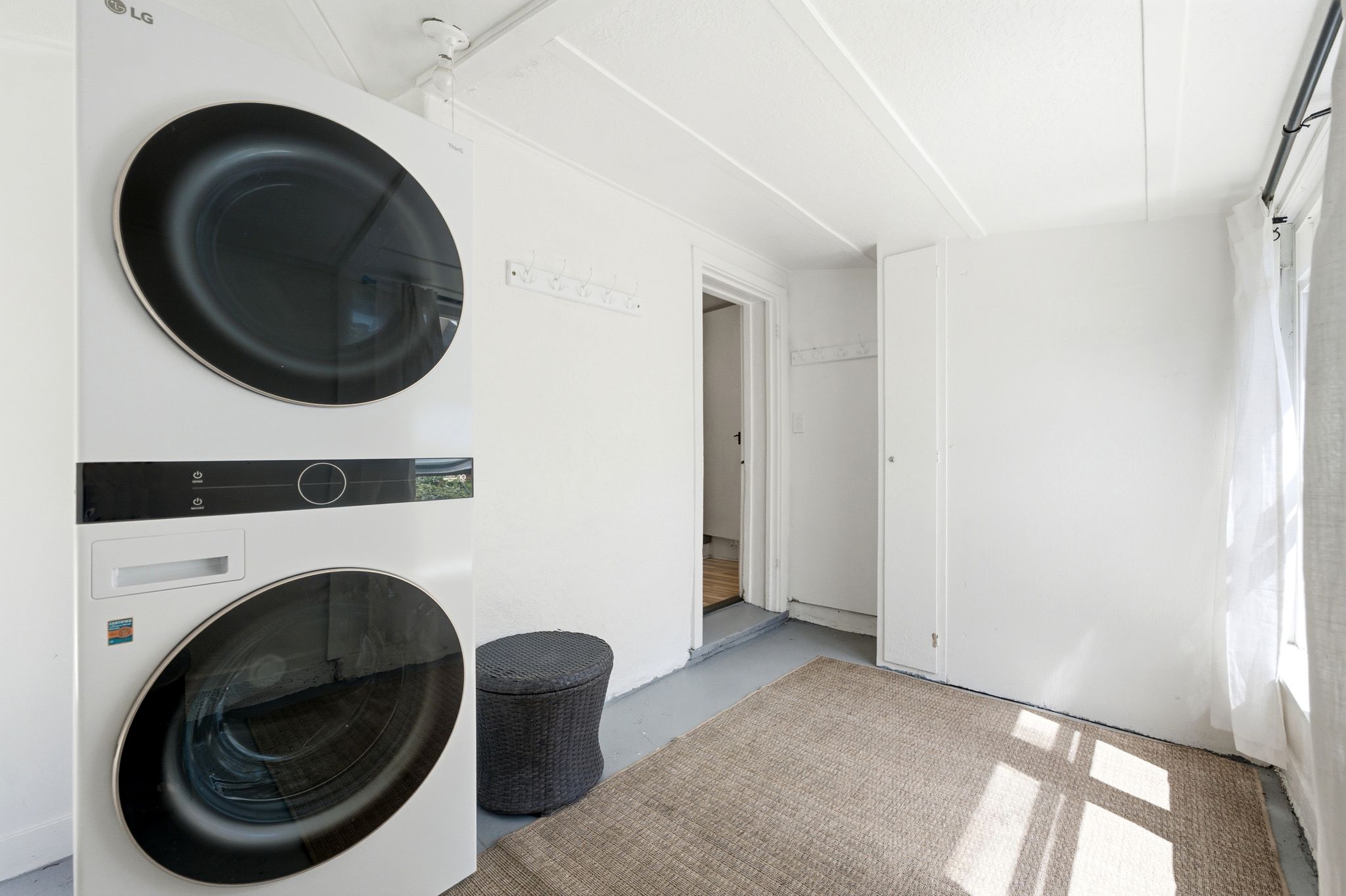 Dedicated laundry area featuring a stacked washer and dryer unit, bright white walls, and a recessed ceiling with exposed beams