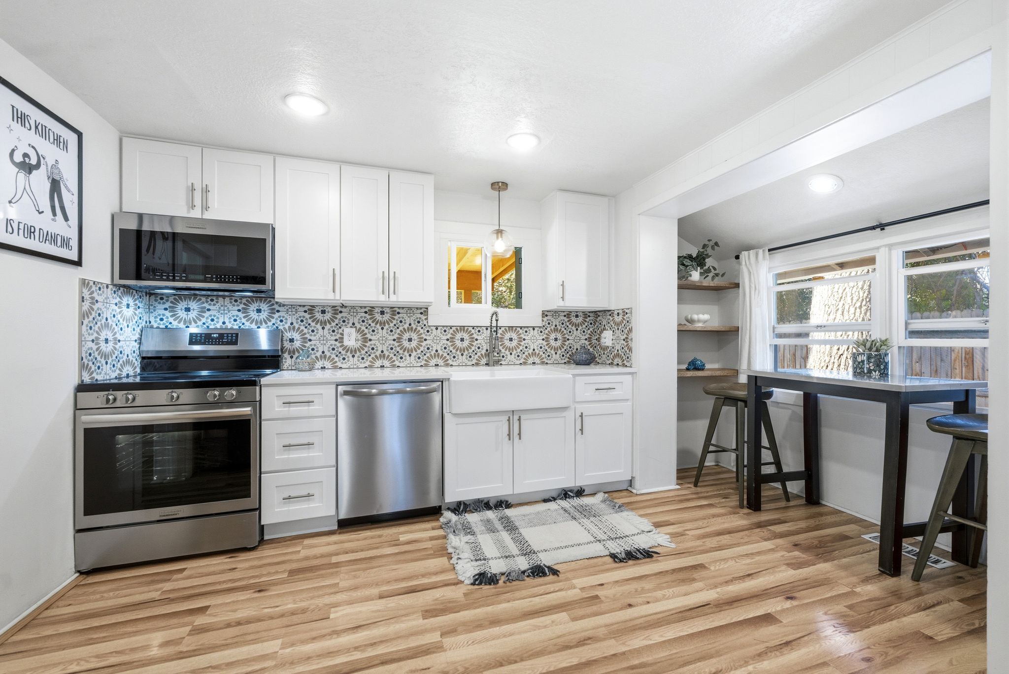 Kitchen featuring white cabinetry, stainless steel appliances, patterned tile backsplash, wood-finish flooring, and a farmhouse sink