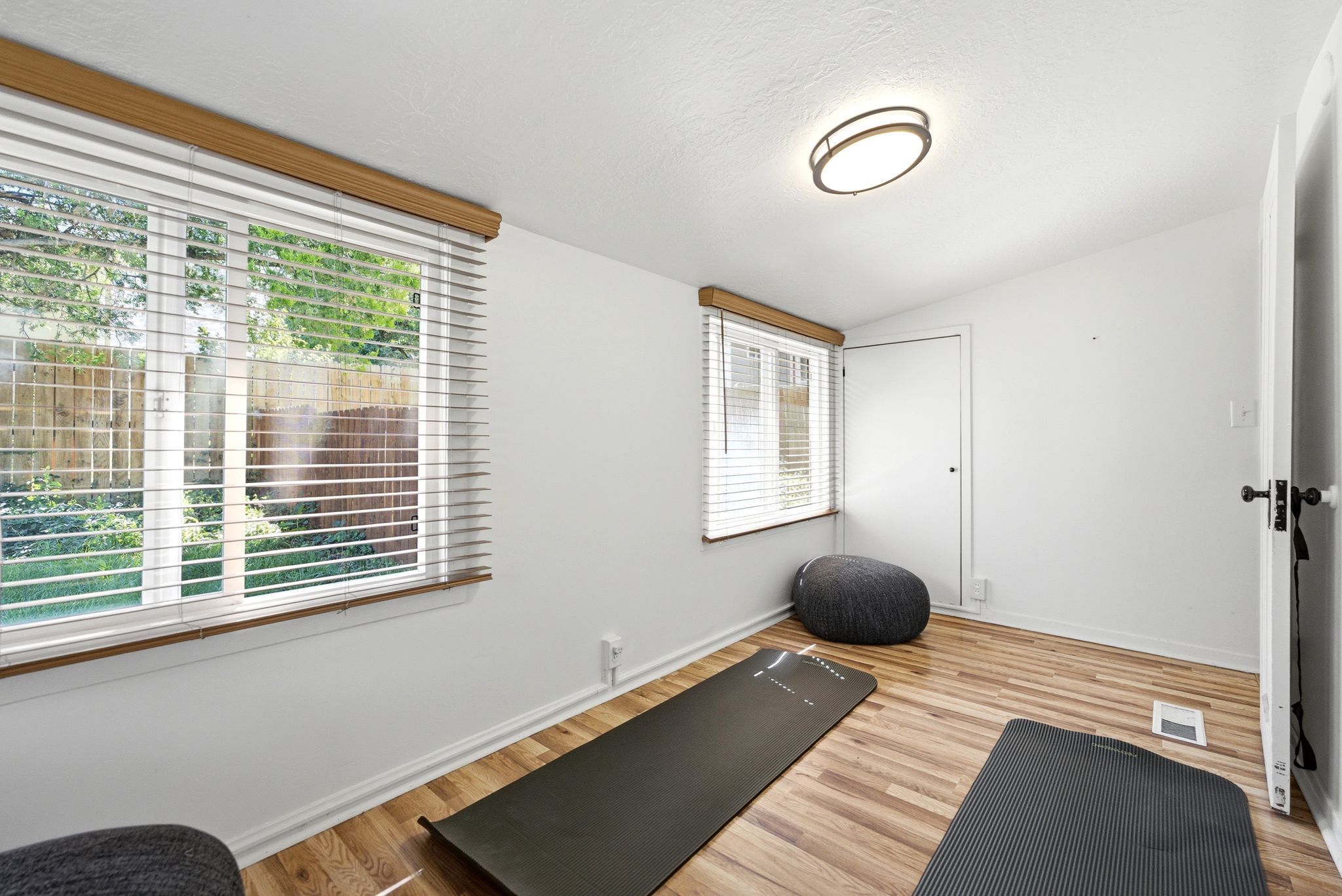 Room with wood-finish flooring, two windows with blinds, a white ceiling, and a flush-mount ceiling light fixture