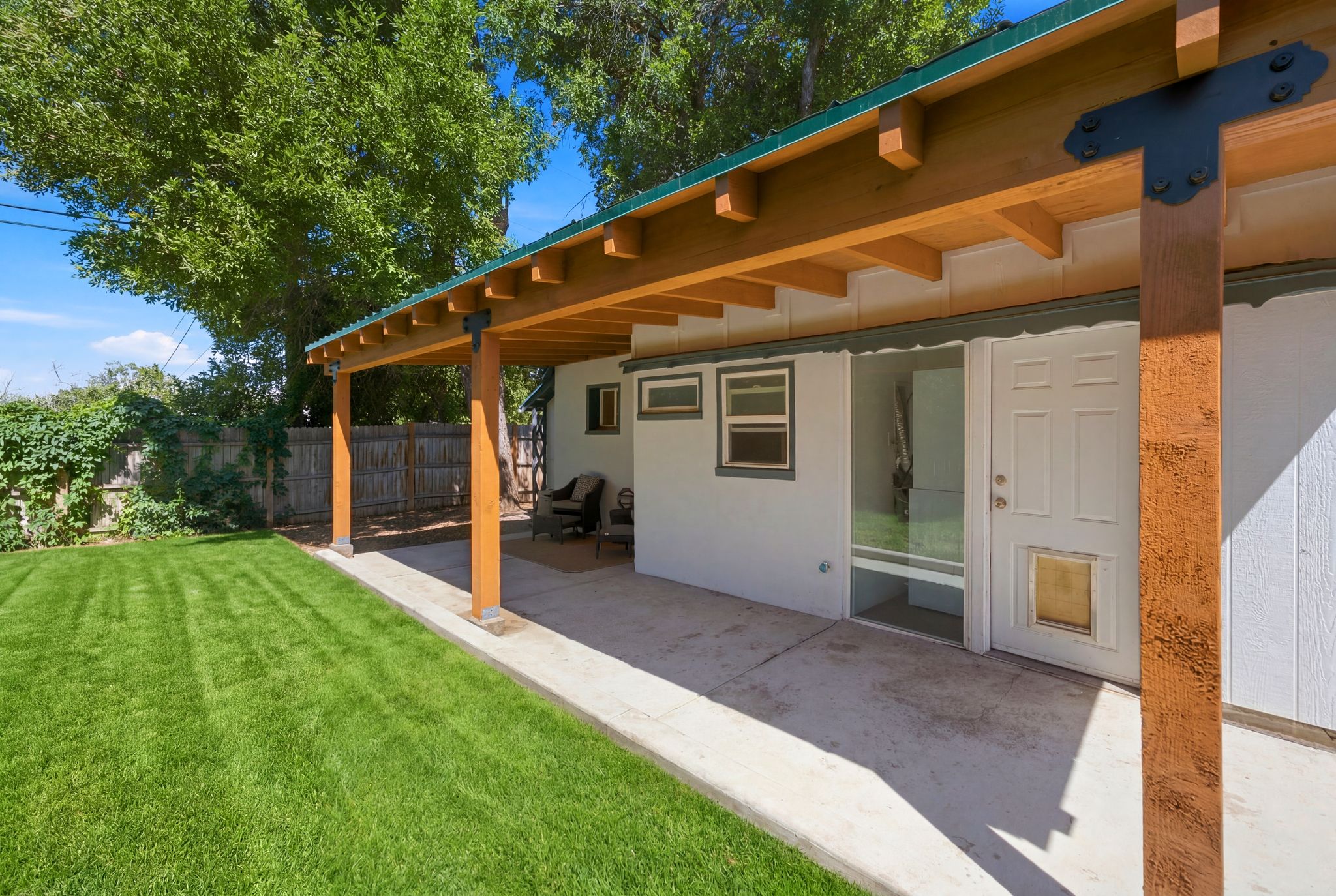 Expansive green lawn with a covered concrete patio featuring exposed wood beams and architectural metal accents