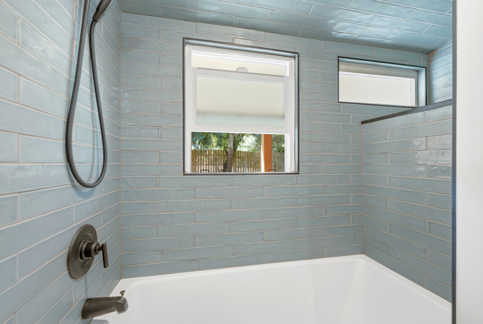 Bathtub with light blue subway tile surround, oil-rubbed bronze fixtures, and two integrated windows