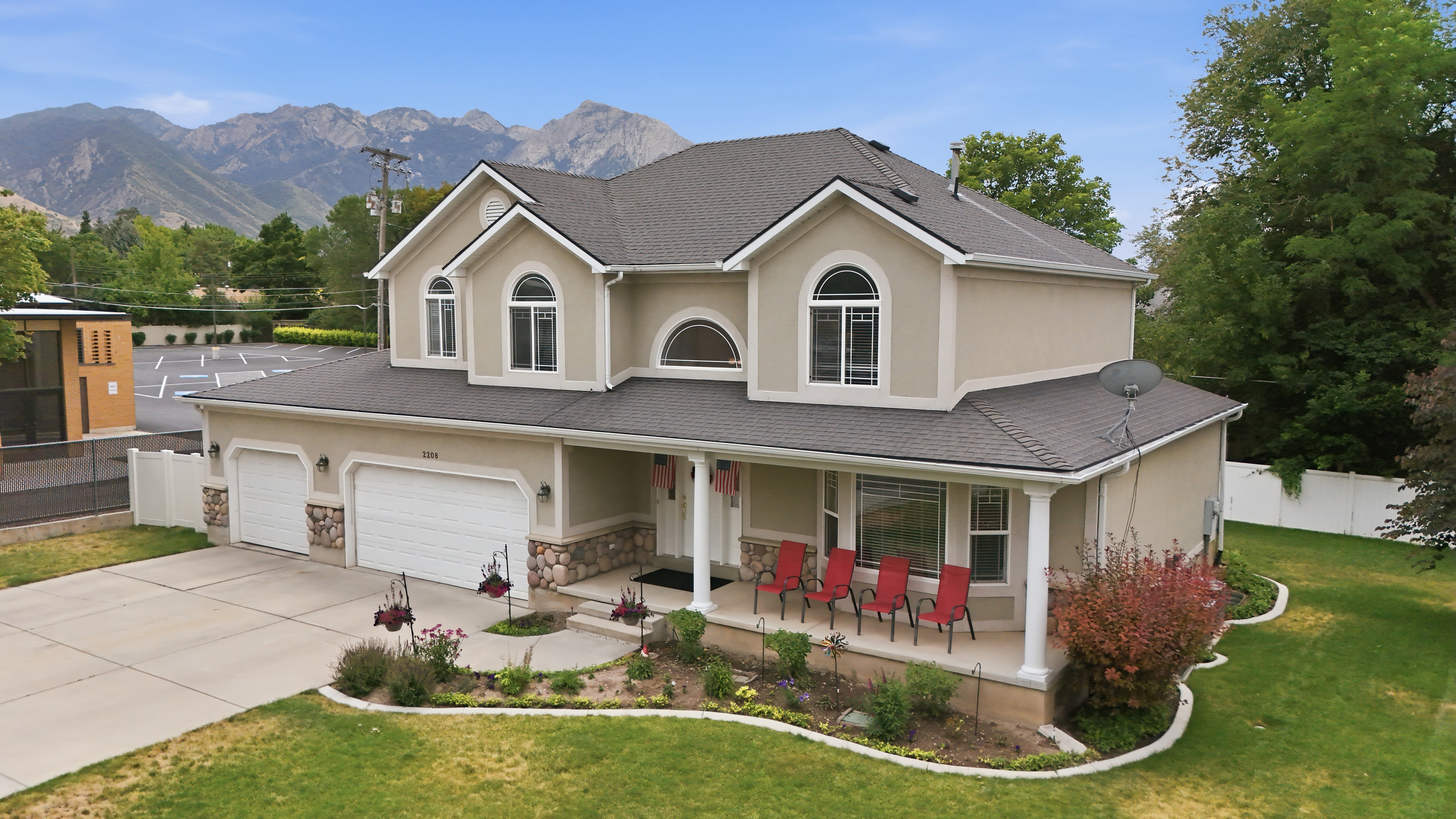 Two-story residence featuring stucco and stone veneer exterior, an attached three-car garage, a covered front porch with white columns, and arched windows