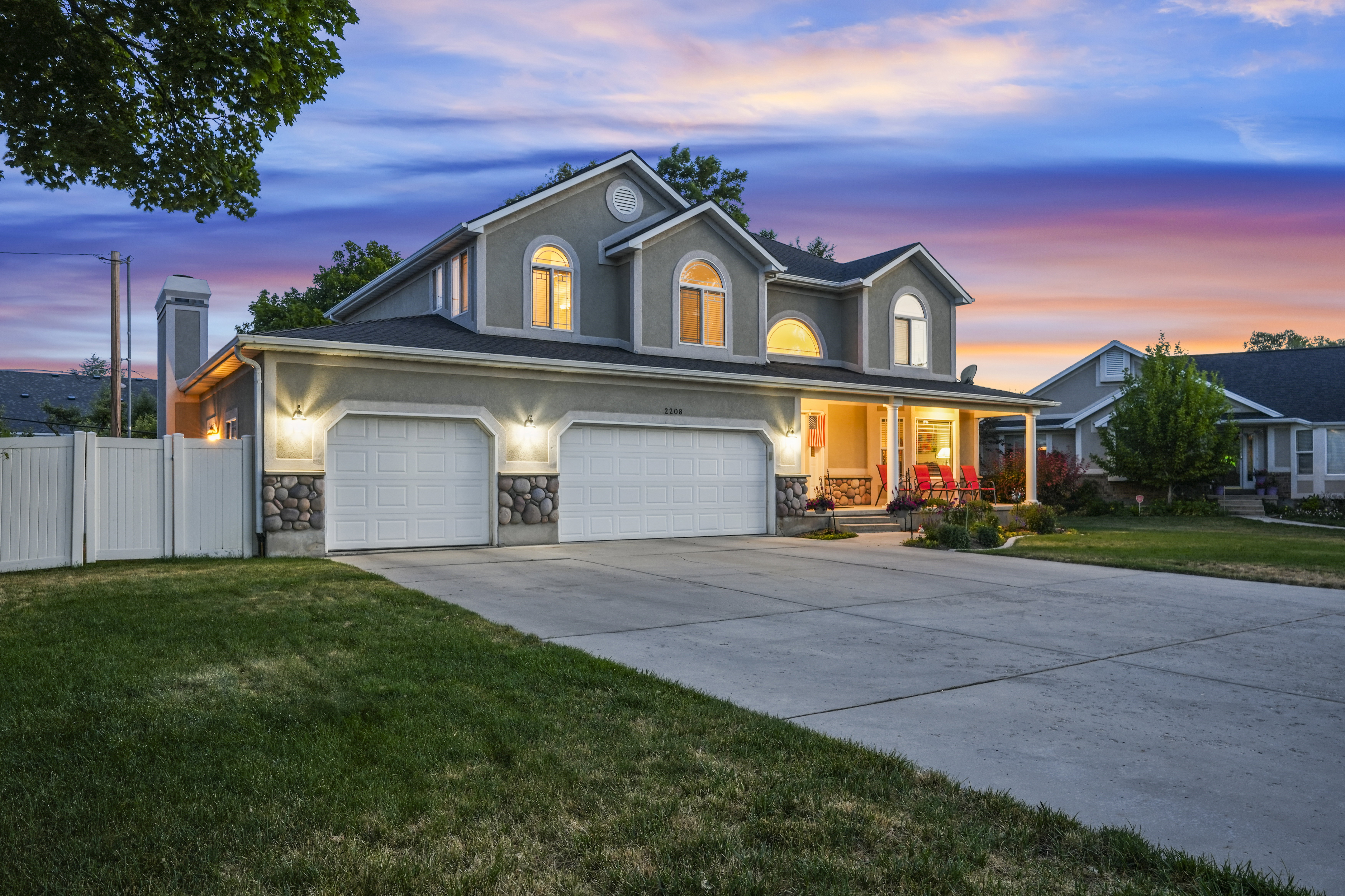 Stucco and stone exterior featuring multiple arched windows, an extended covered front porch, an attached three-car garage, and a concrete driveway