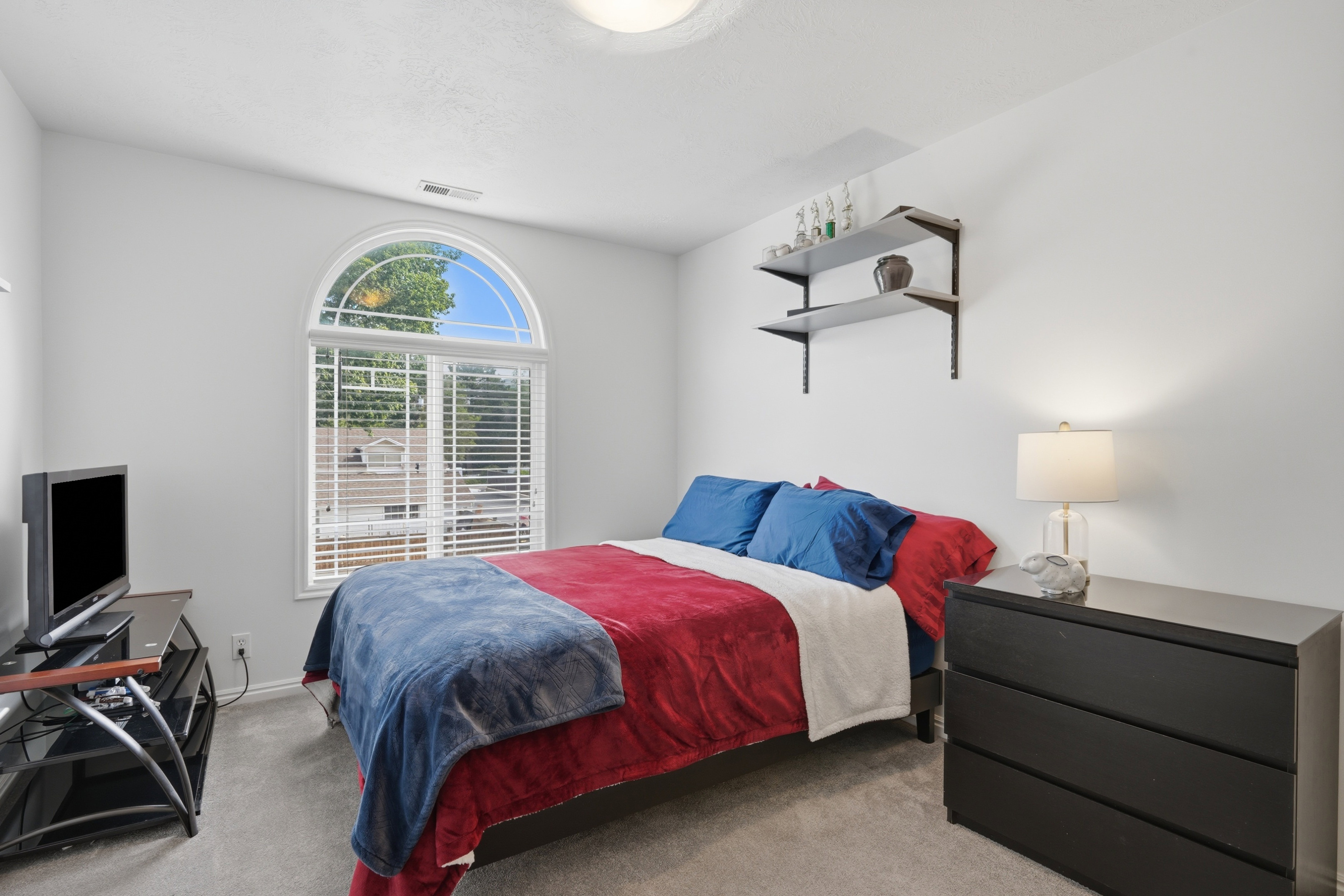 Bedroom featuring a large arched window with blinds, light gray carpet, and white walls