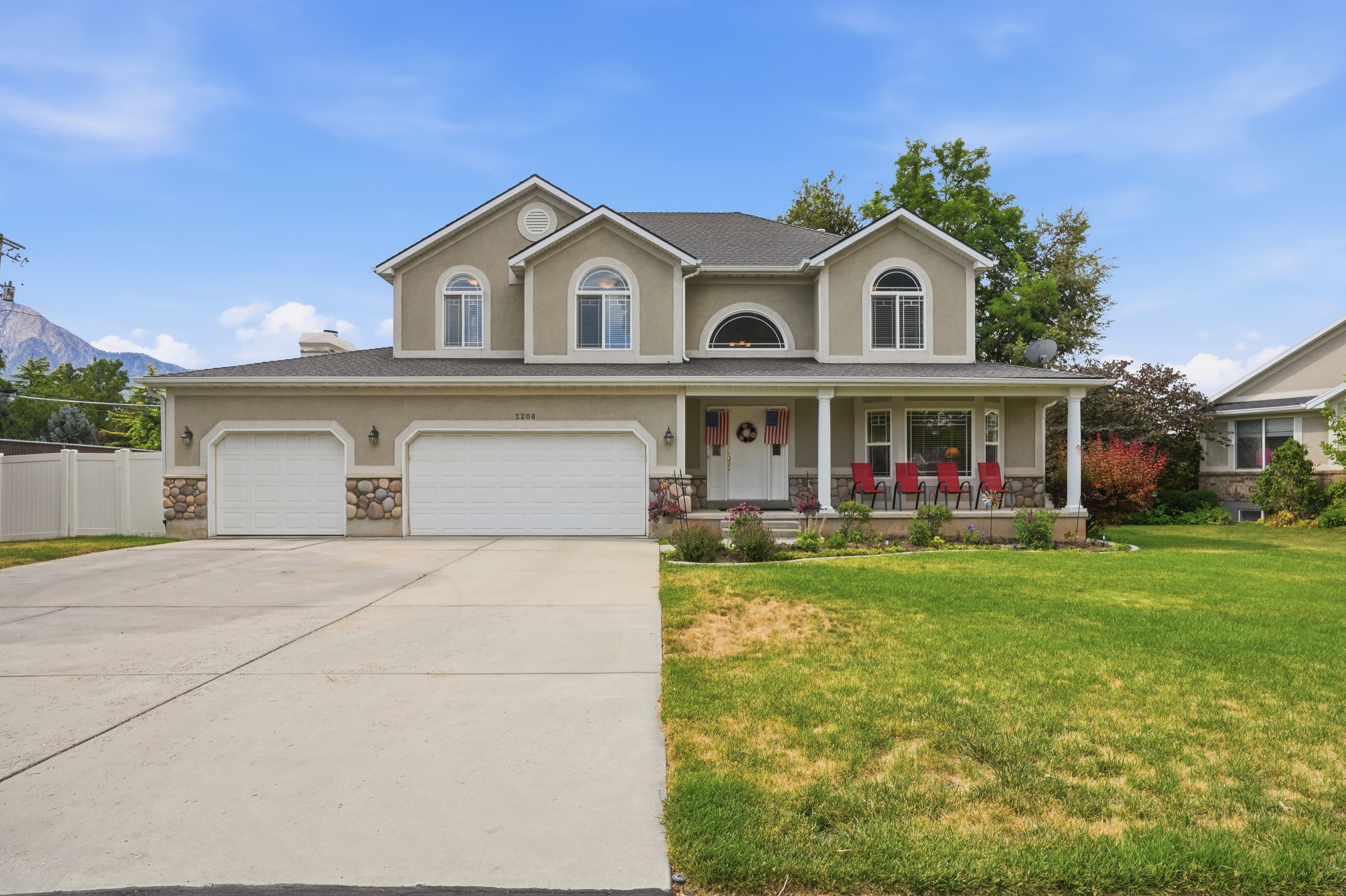 Two-story stucco residence featuring a covered front porch with white columns, a three-car garage with stone accents, a landscaped front yard, and a paved driveway