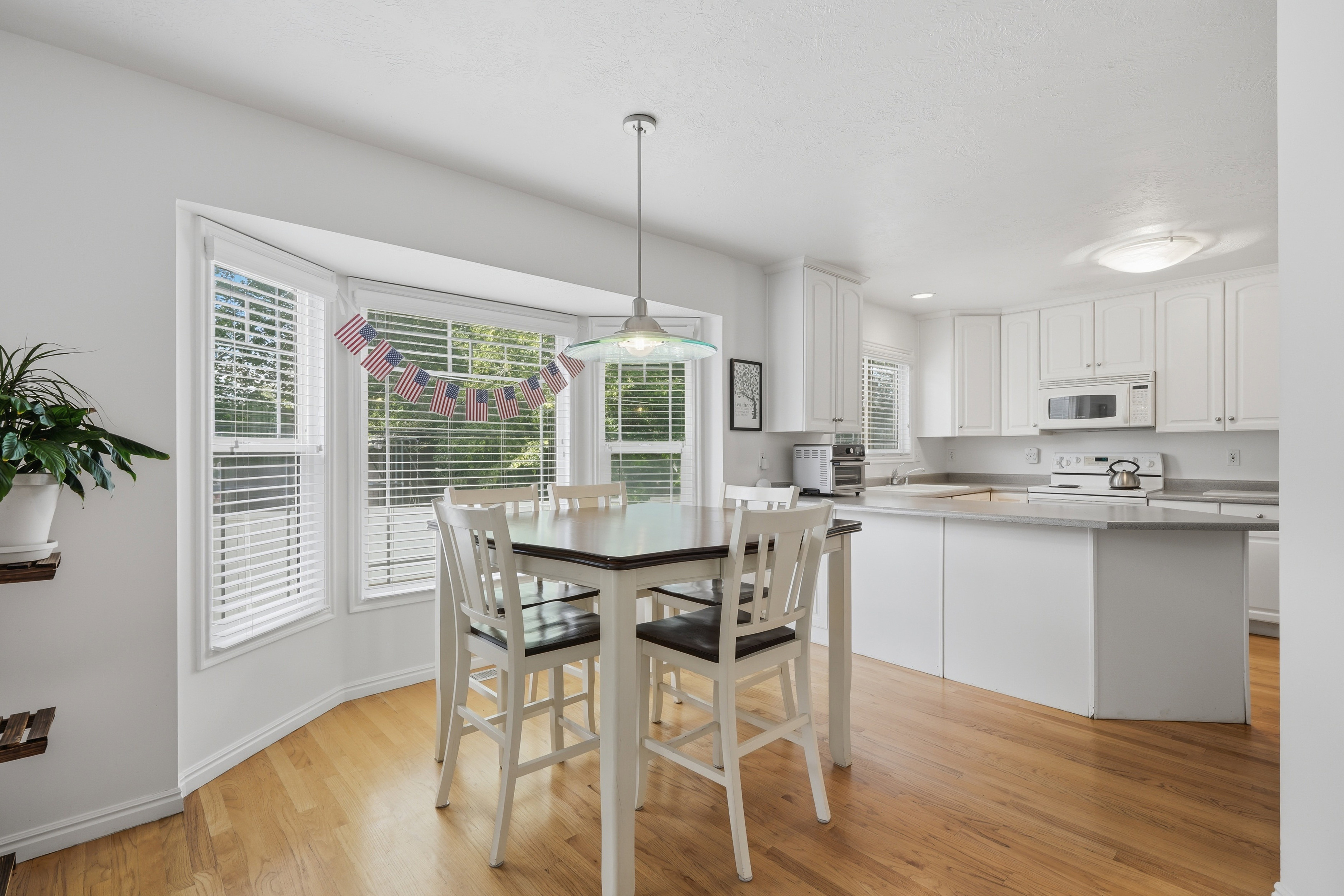 Eat-in kitchen featuring a bay window, wood-finish flooring, white cabinetry, a white appliance suite, and a breakfast bar