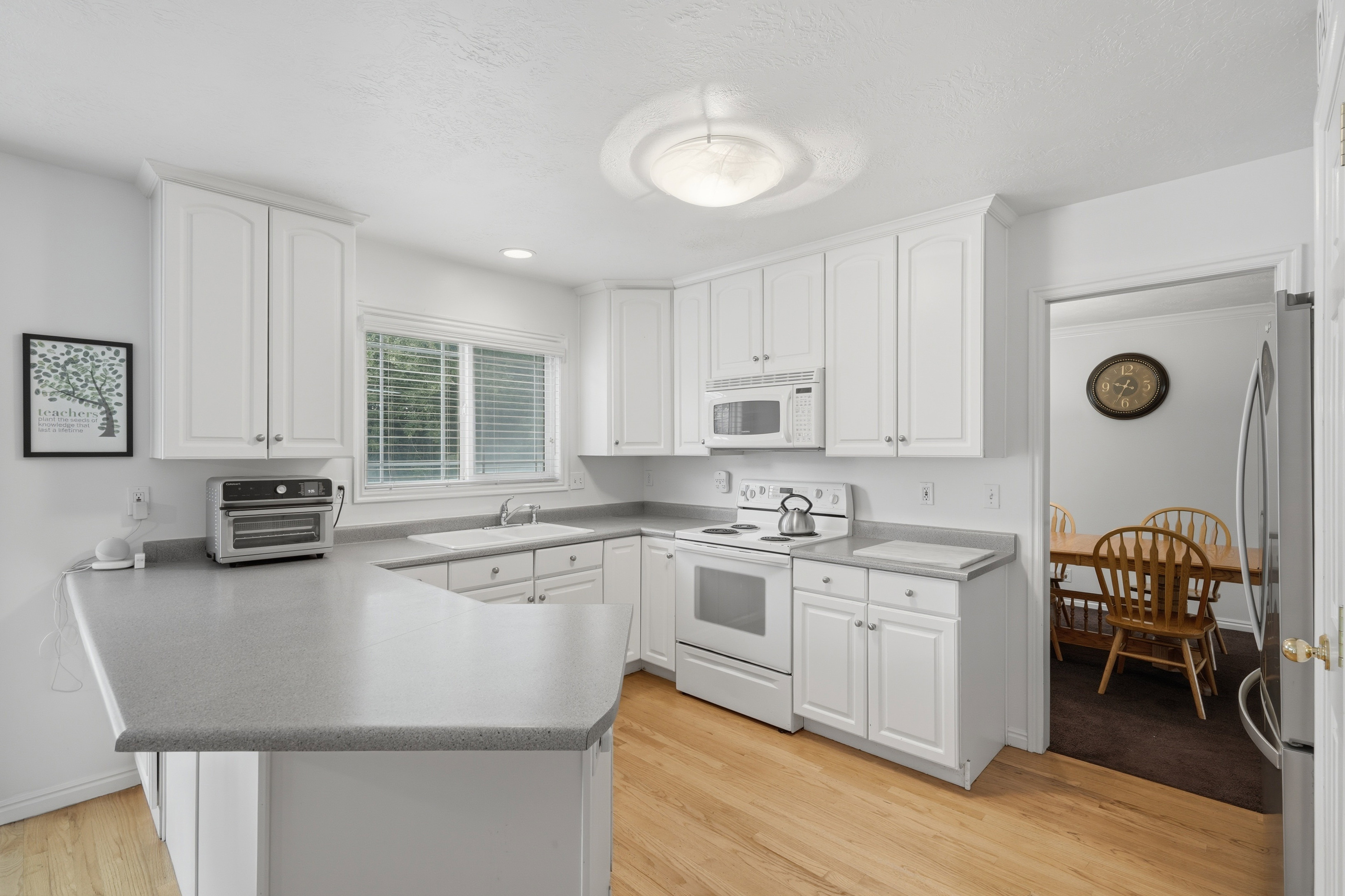 Bright kitchen featuring white cabinetry, light-toned countertops, a white range, and wood-finish flooring