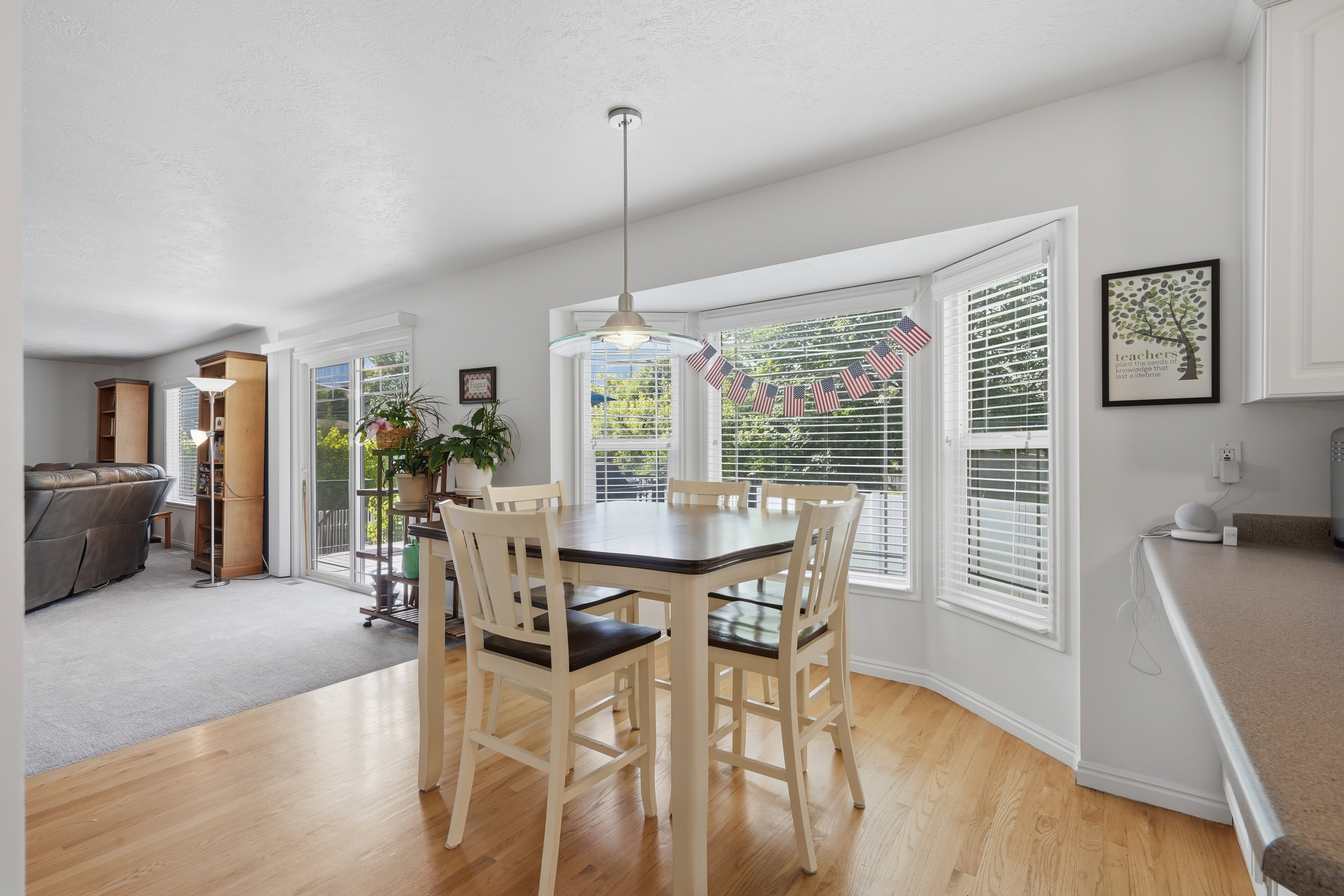Bay window dining area featuring blonde wood-finish flooring, a pendant light fixture, and white window blinds
