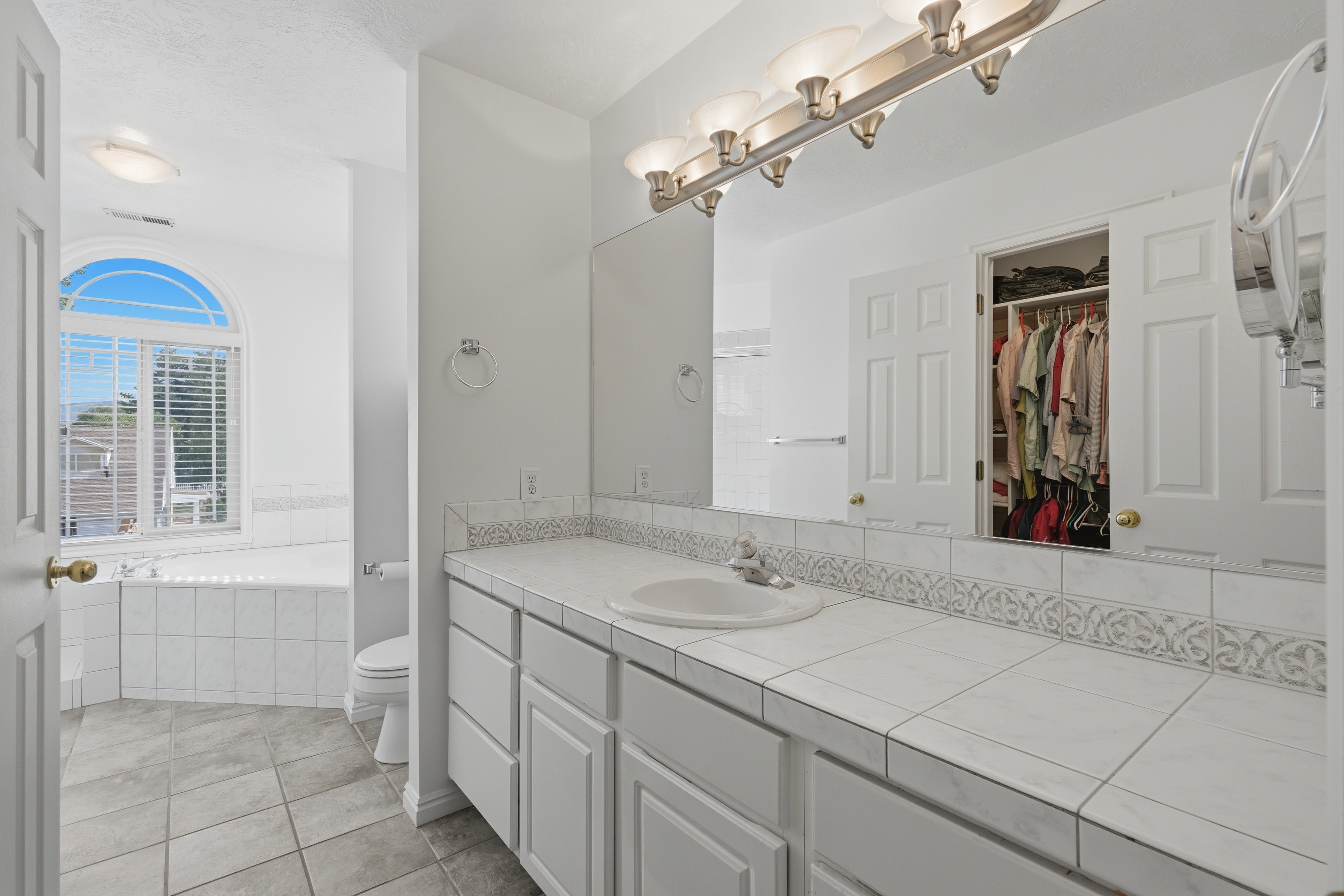 Bathroom featuring a broad vanity with tiled countertop, integrated sink, and an expansive mirror