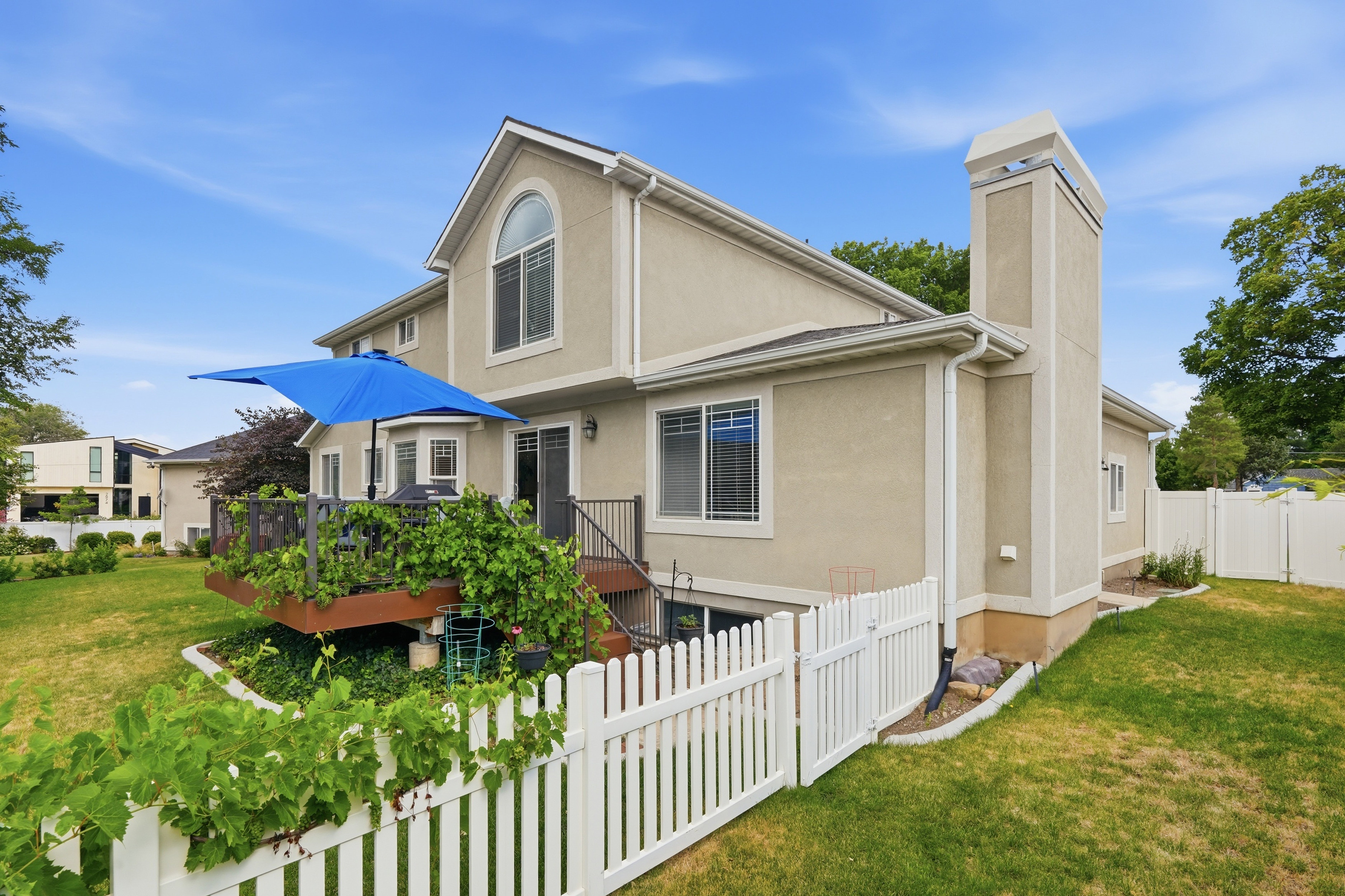 Expansive backyard featuring a multi-level deck, stucco exterior, white picket fence, and a tall chimney structure