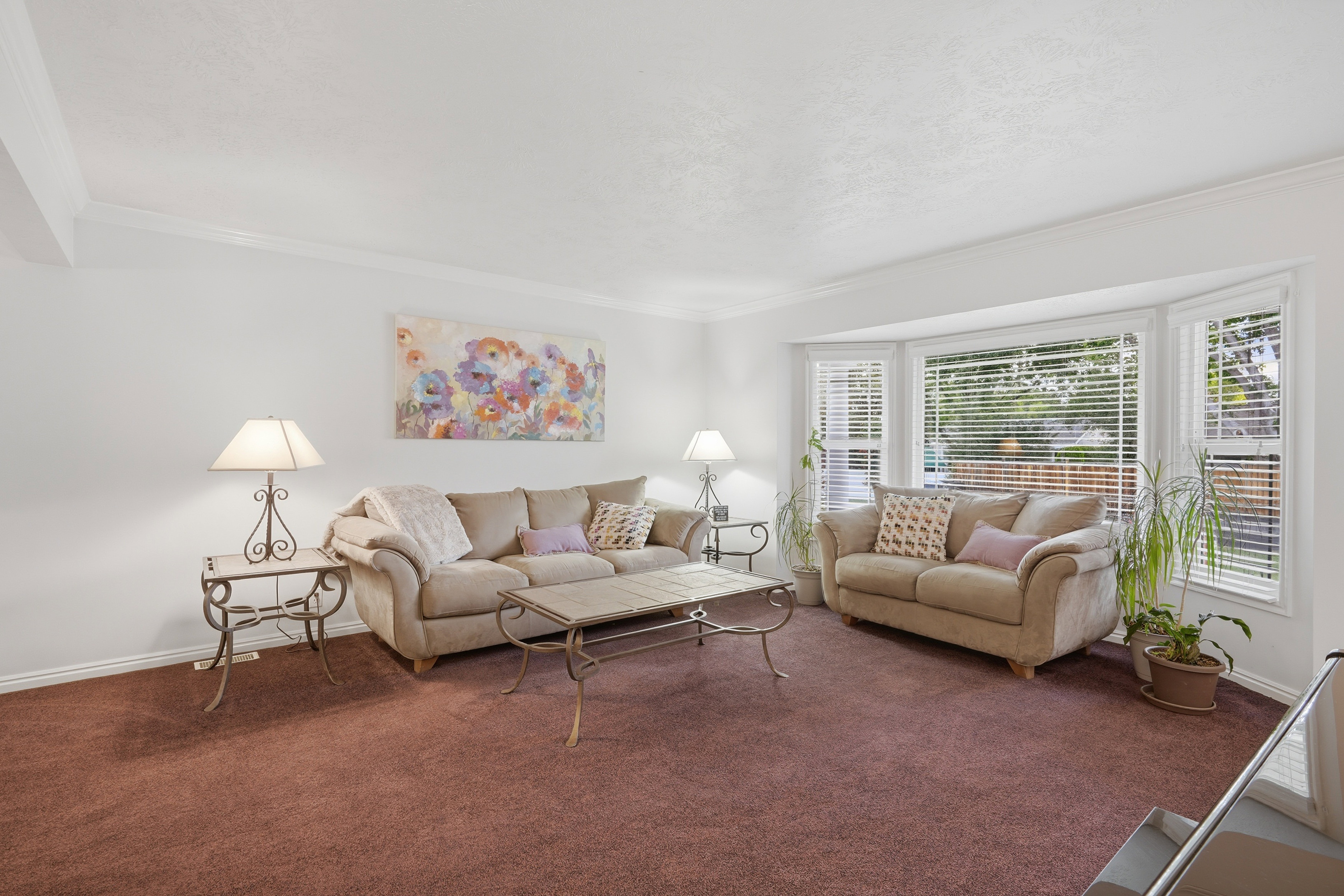 Spacious living area featuring a large bay window, crown molding, white walls, and plush carpeting