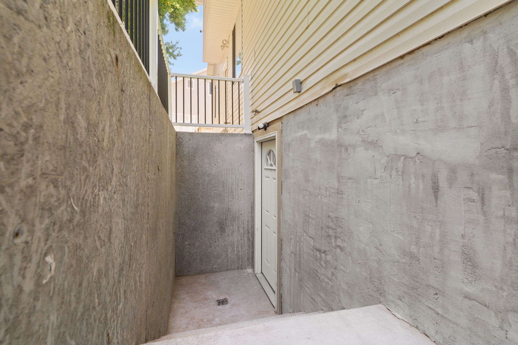 Exterior entry featuring a white door with an arched window insert, surrounded by a concrete foundation and light-colored siding