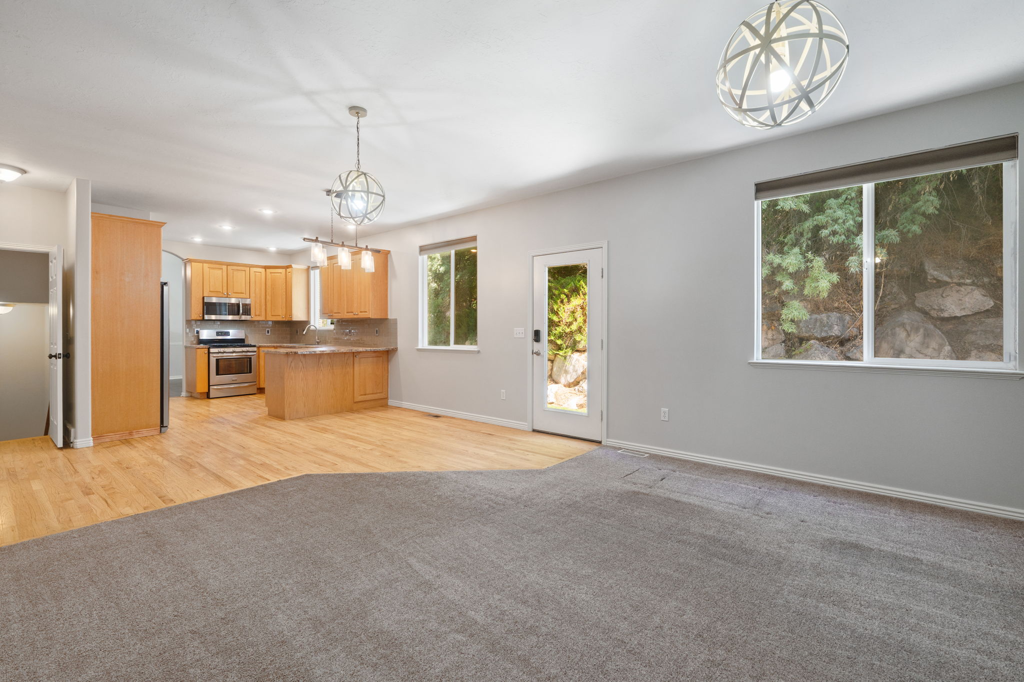 Open-concept living area with mixed flooring, featuring a kitchen with wood cabinetry and stainless steel appliances