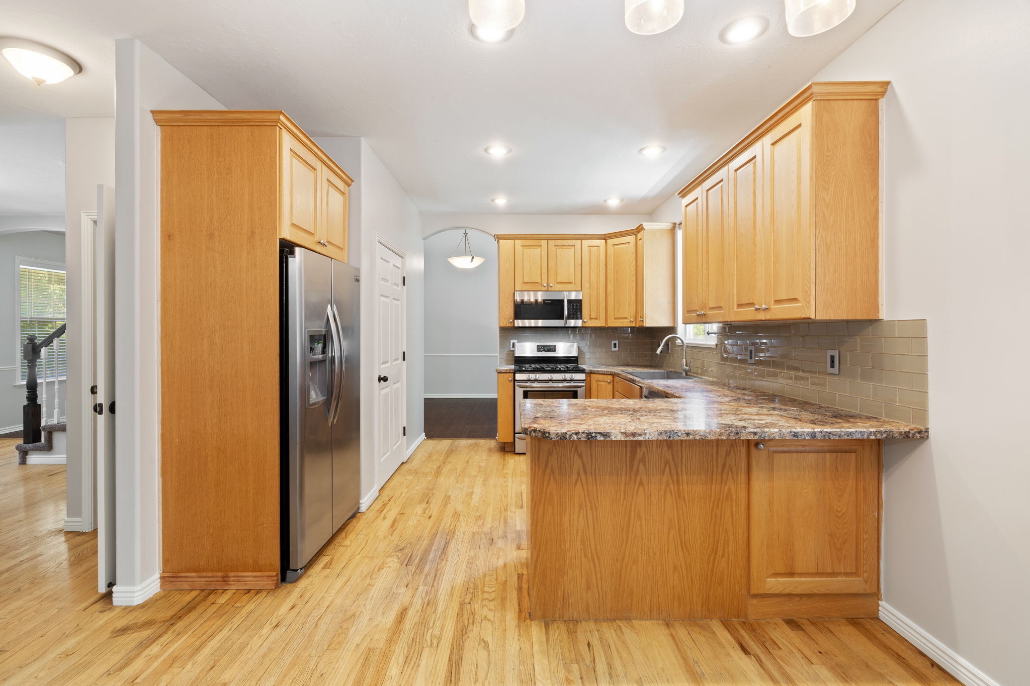 Kitchen featuring wood-finish flooring, light wood cabinetry, stainless steel appliances, and a tile backsplash