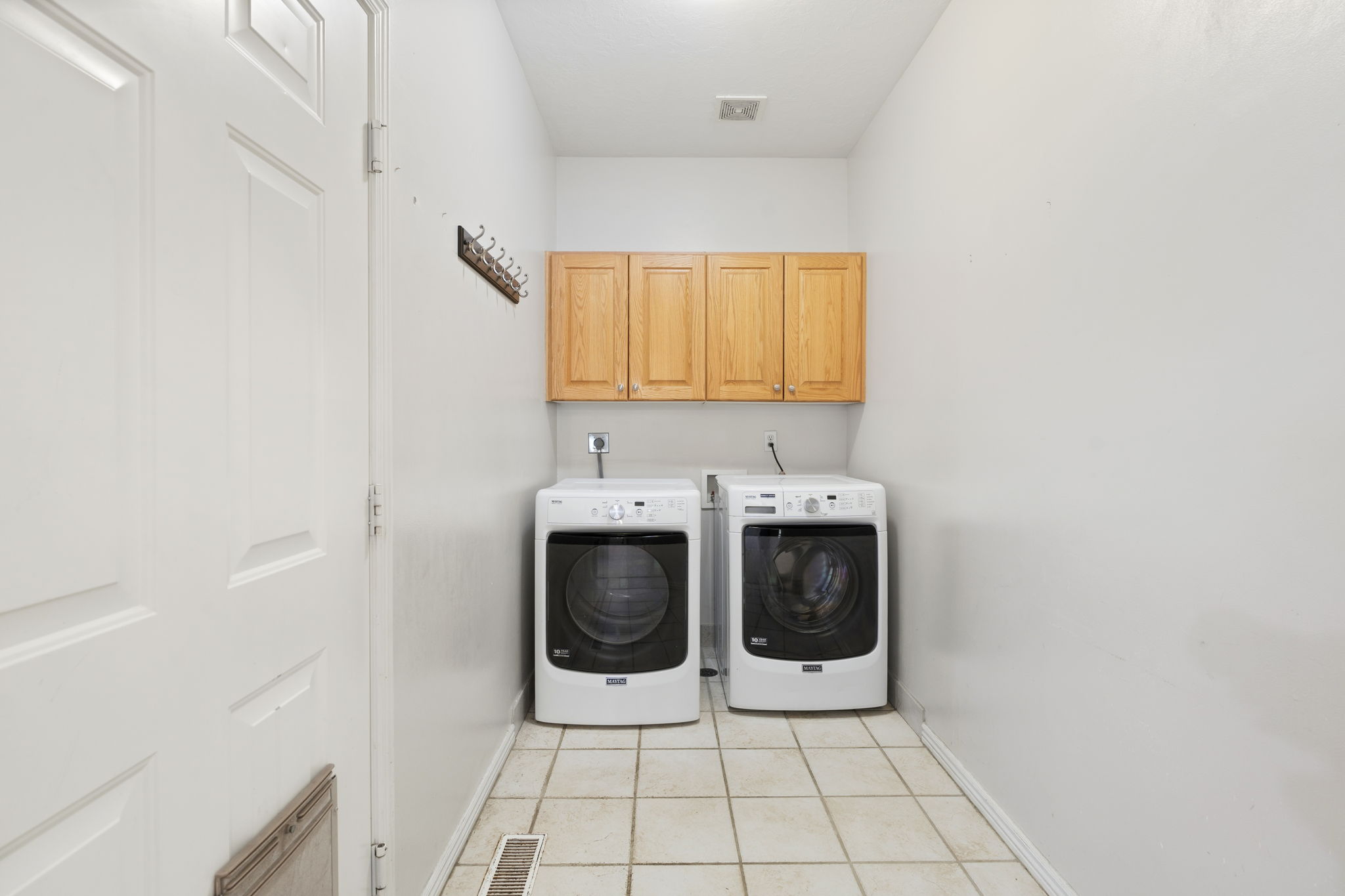Utility room featuring light wood-finish cabinetry, tile flooring, and a paneled door