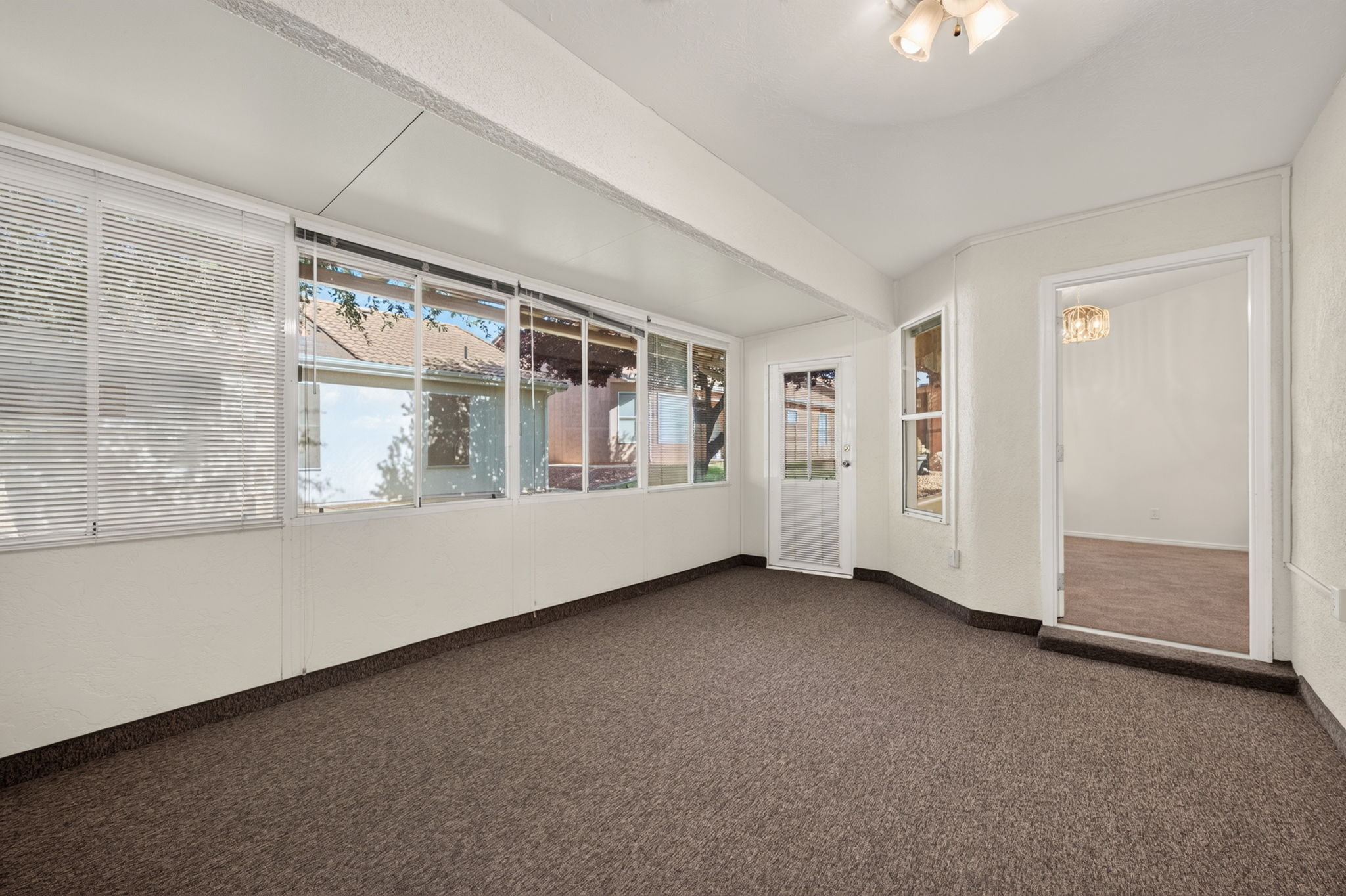 Enclosed sunroom featuring multiple windows with blinds, a glass-panel exterior door, and durable carpet flooring