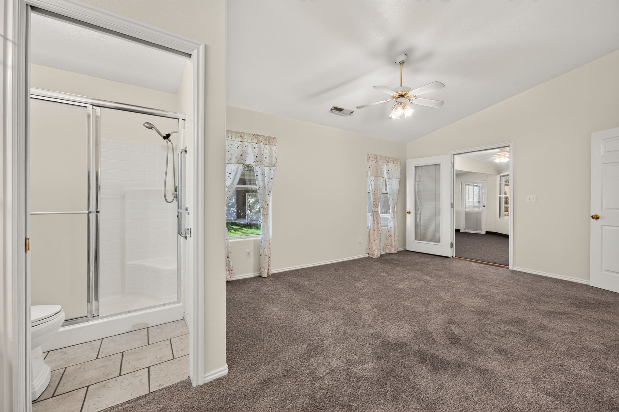 Spacious carpeted room with vaulted ceilings and a ceiling fan