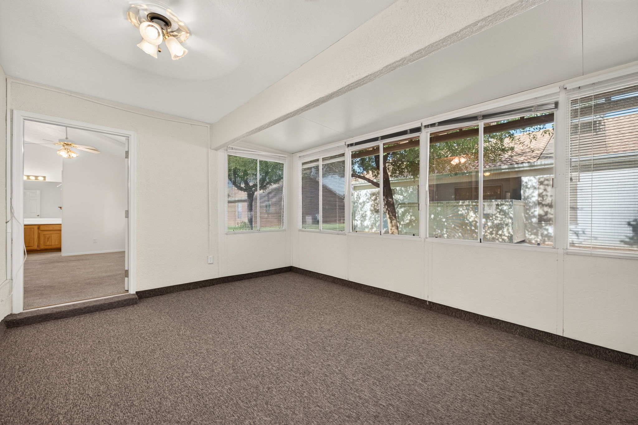 Sunroom featuring expansive windows, neutral wall tones, textured carpet flooring, and a ceiling fan with integrated lighting