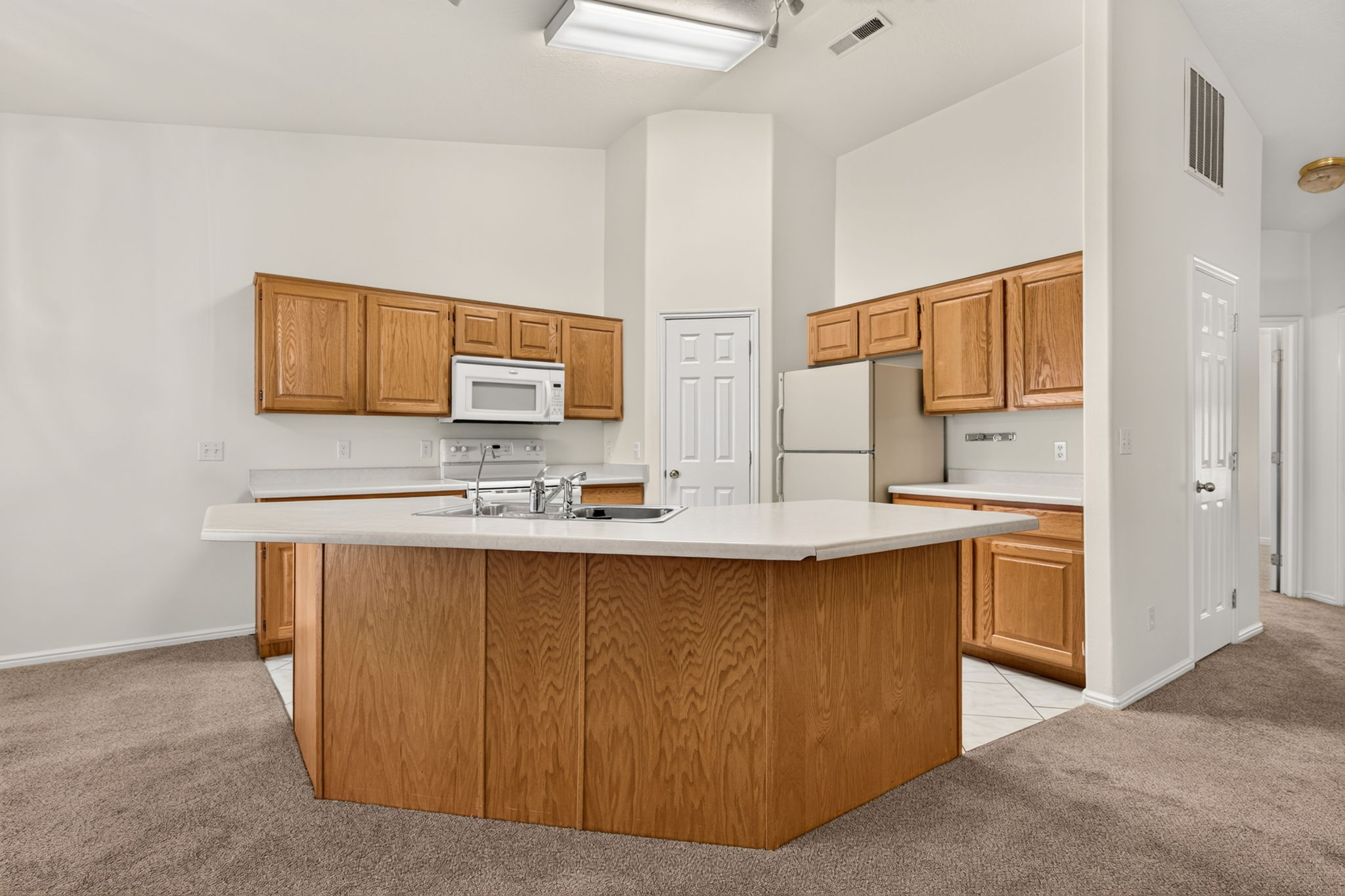 Open-concept kitchen featuring oak cabinetry, light-toned countertops, and a central island with an integrated sink