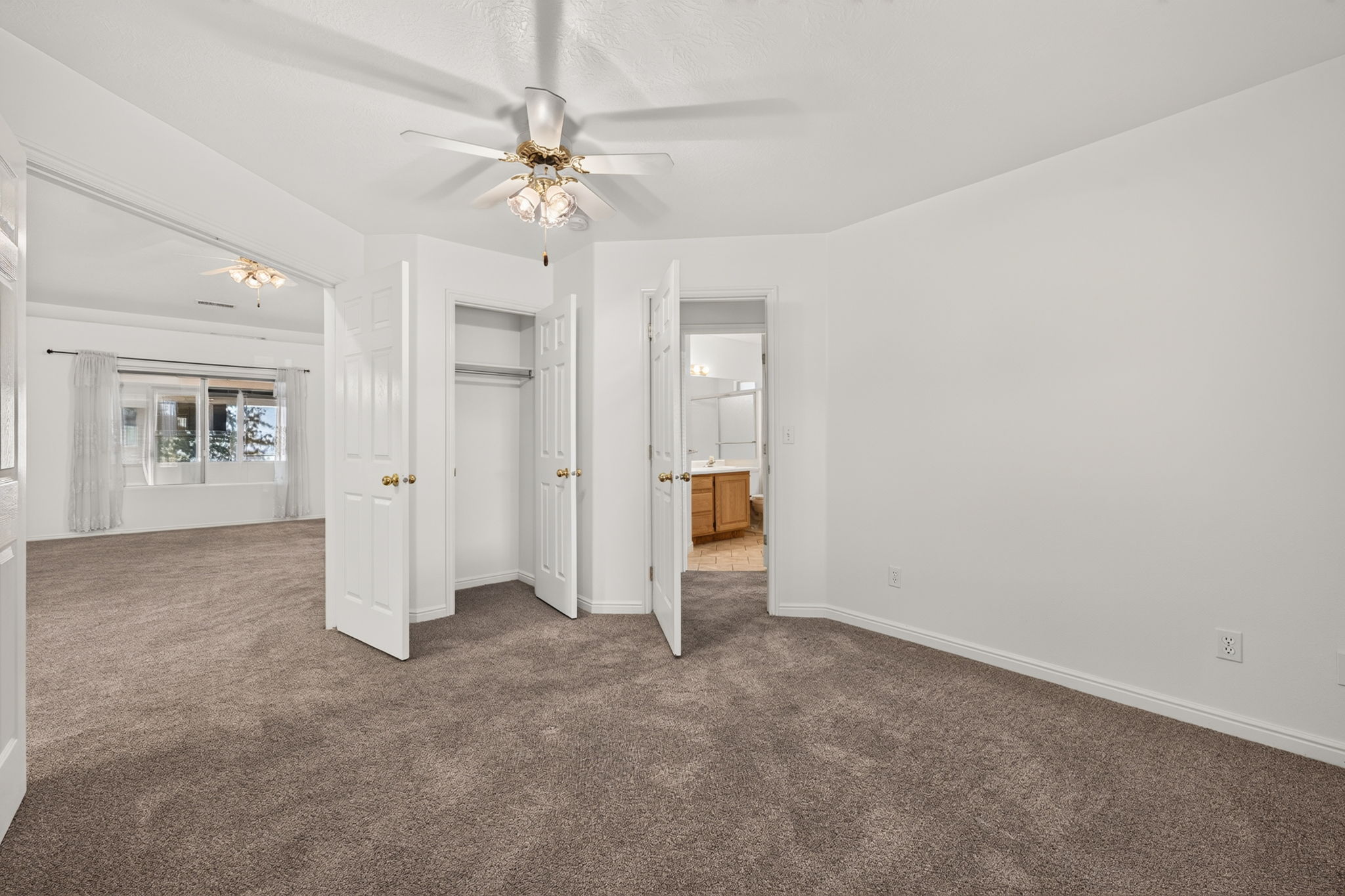Carpeted room with white walls, a ceiling fan, and white bi-fold closet doors