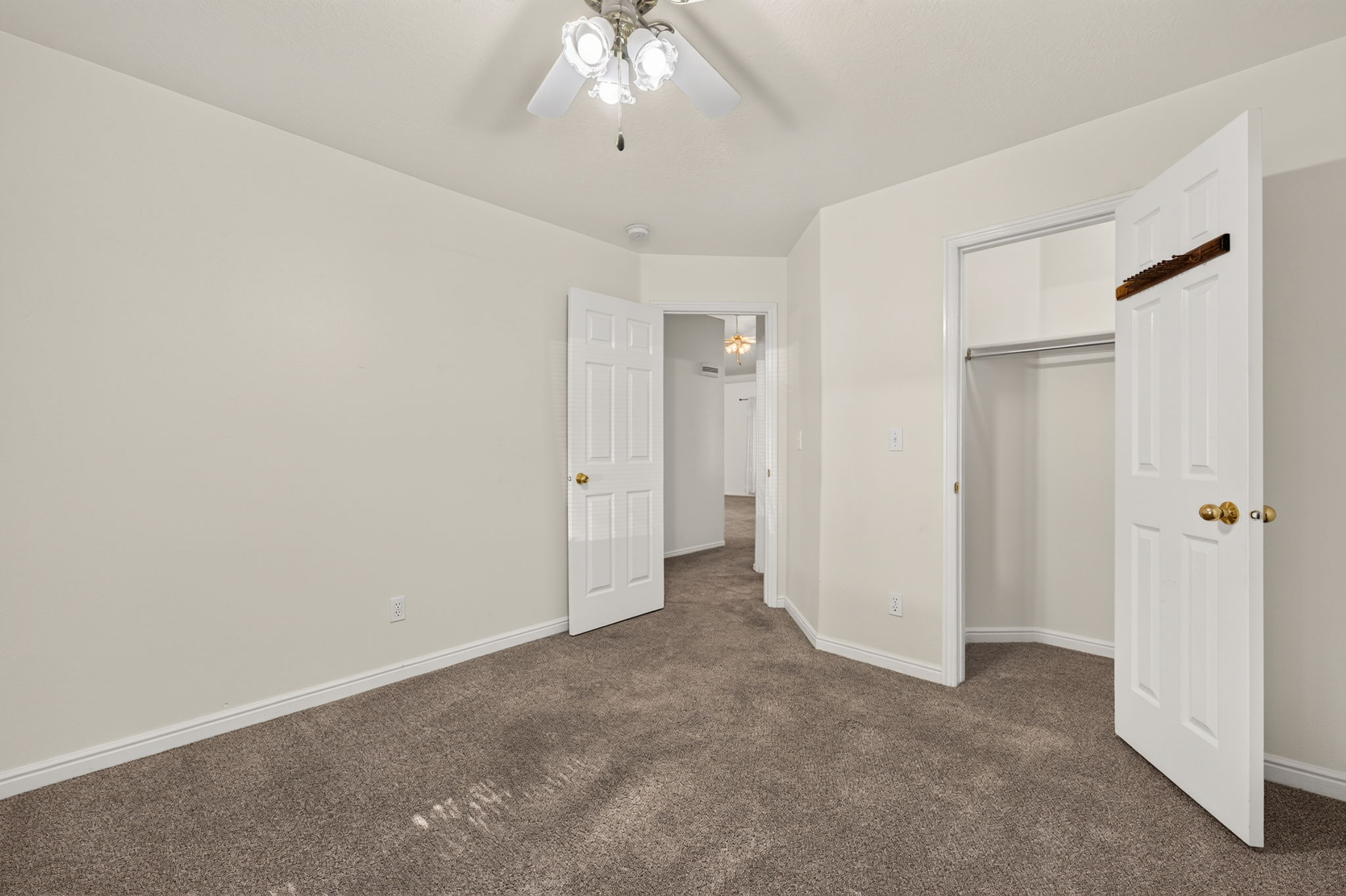 Carpeted interior room featuring a ceiling fan with light fixture, white trim, and a bi-fold closet with shelving