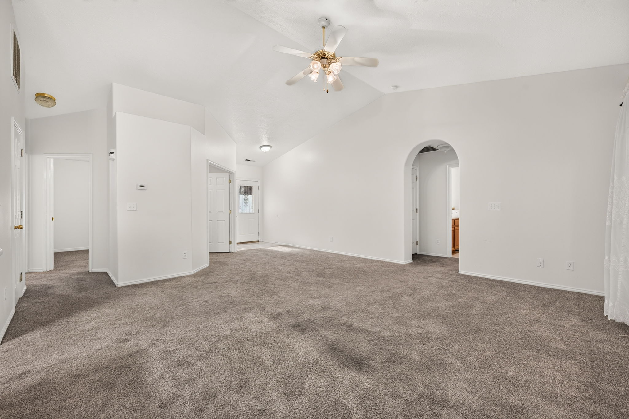 Spacious room featuring vaulted ceilings, a ceiling fan, plush gray carpeting, and an arched doorway