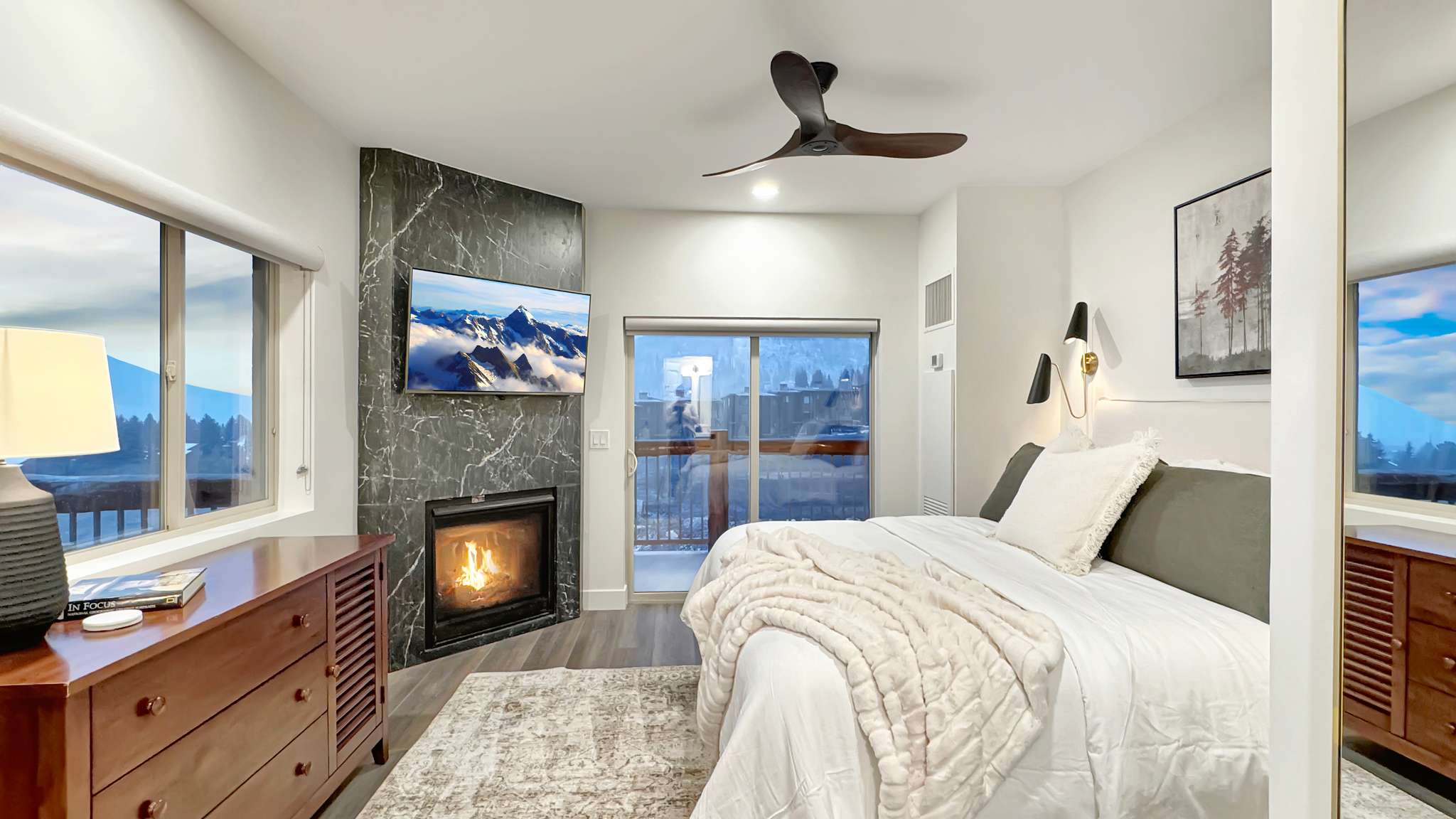 Corner fireplace with marble-look surround, mounted television, and a ceiling fan