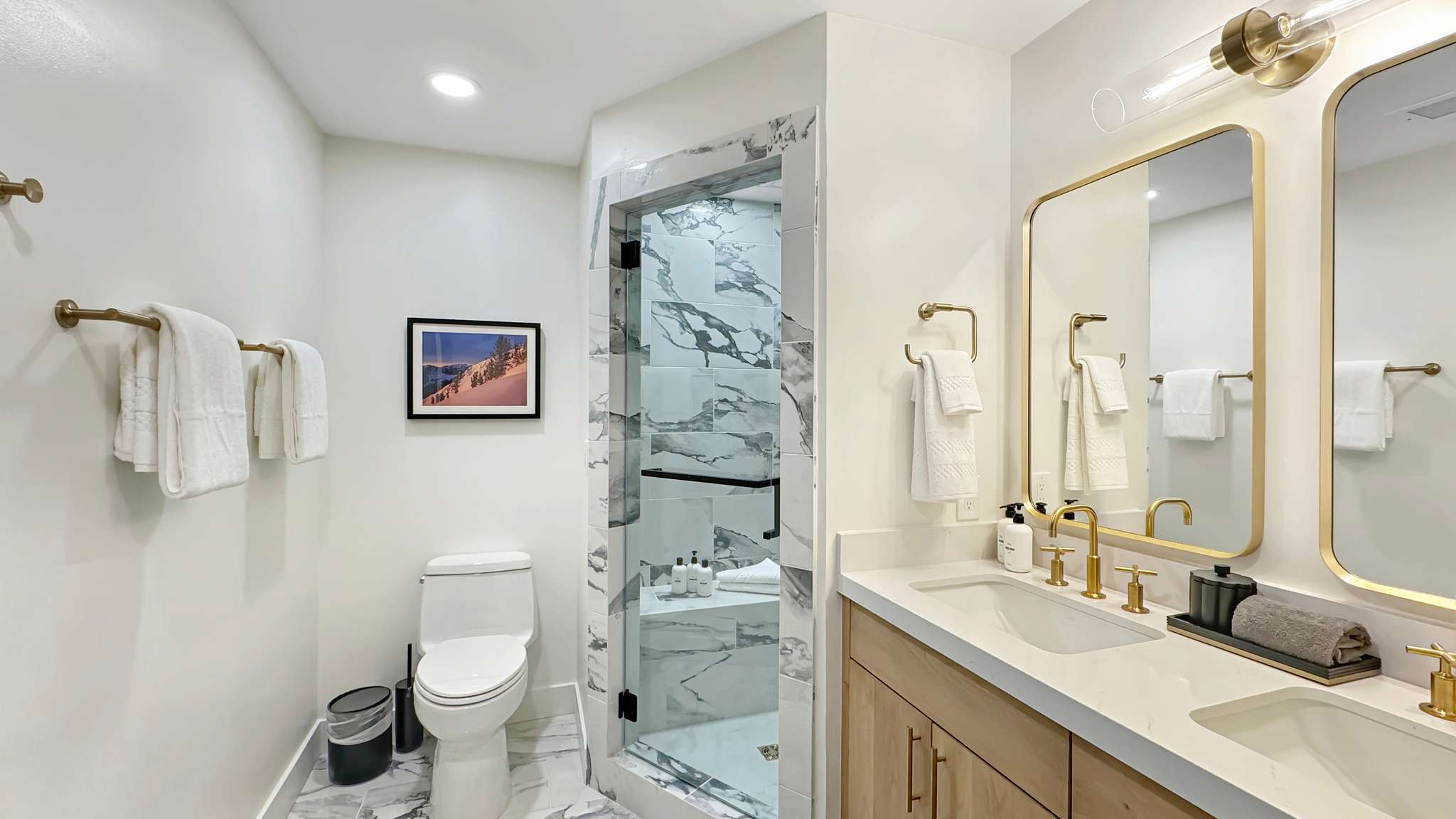 Contemporary bathroom featuring a double vanity with stone countertops and undermount sinks, gold-tone fixtures, and dual framed mirrors