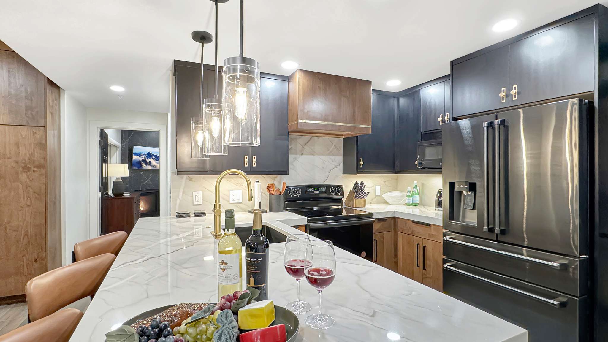 Kitchen featuring a large island with a waterfall edge, pendant lighting, black cabinetry with gold-toned hardware, stainless steel appliances, and a marble-patterned backsplash