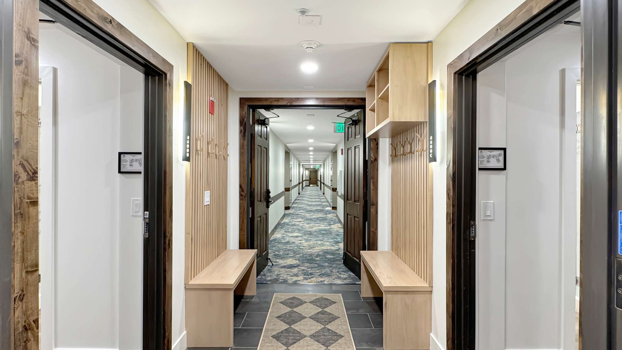 Hallway entry featuring custom built-in bench seating, vertical wood slat wall paneling, built-in shelving, dark wood trim, and wall-mounted sconce lighting